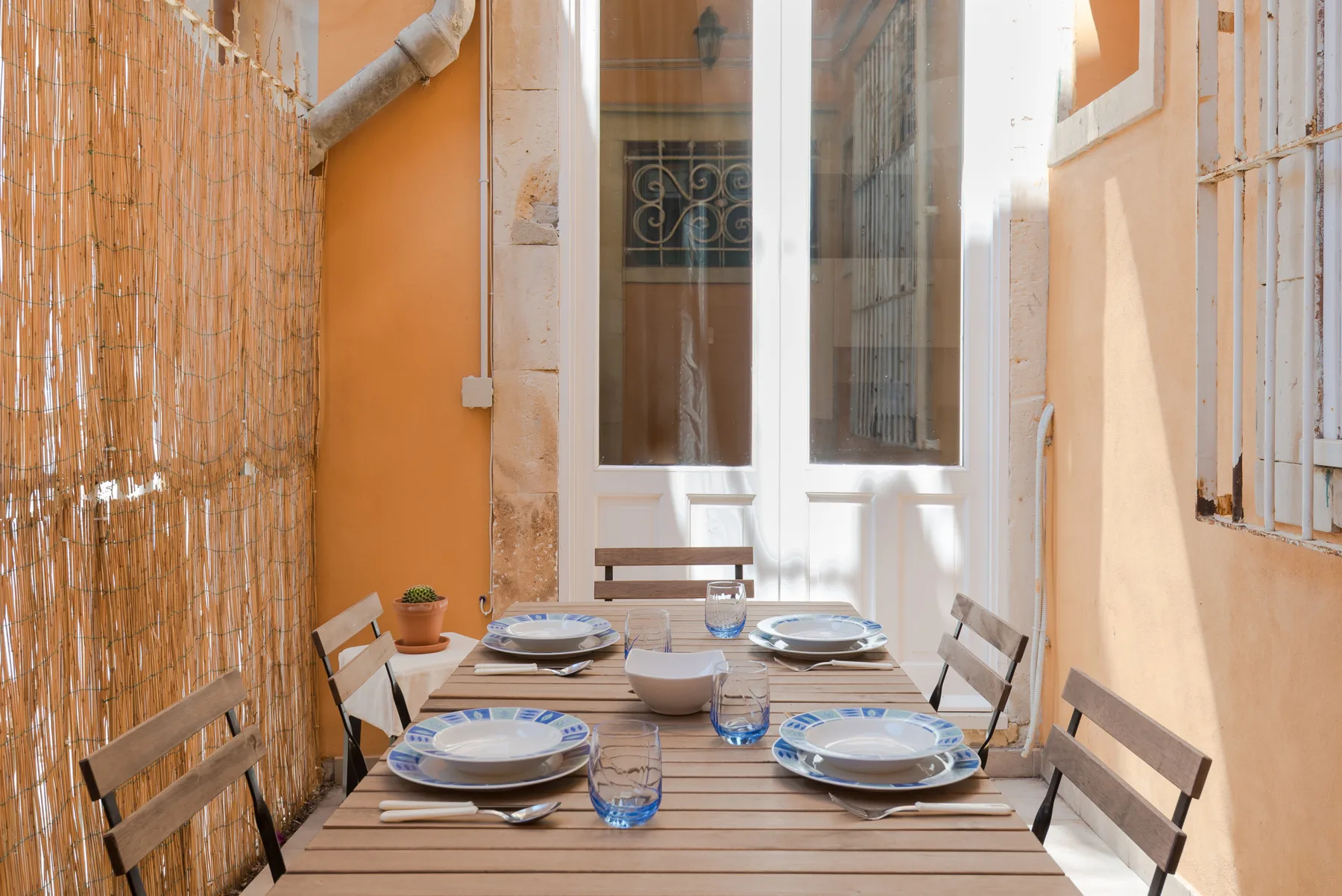 Una zona de comedor al aire libre con una mesa de madera puesta con platos y vasos.