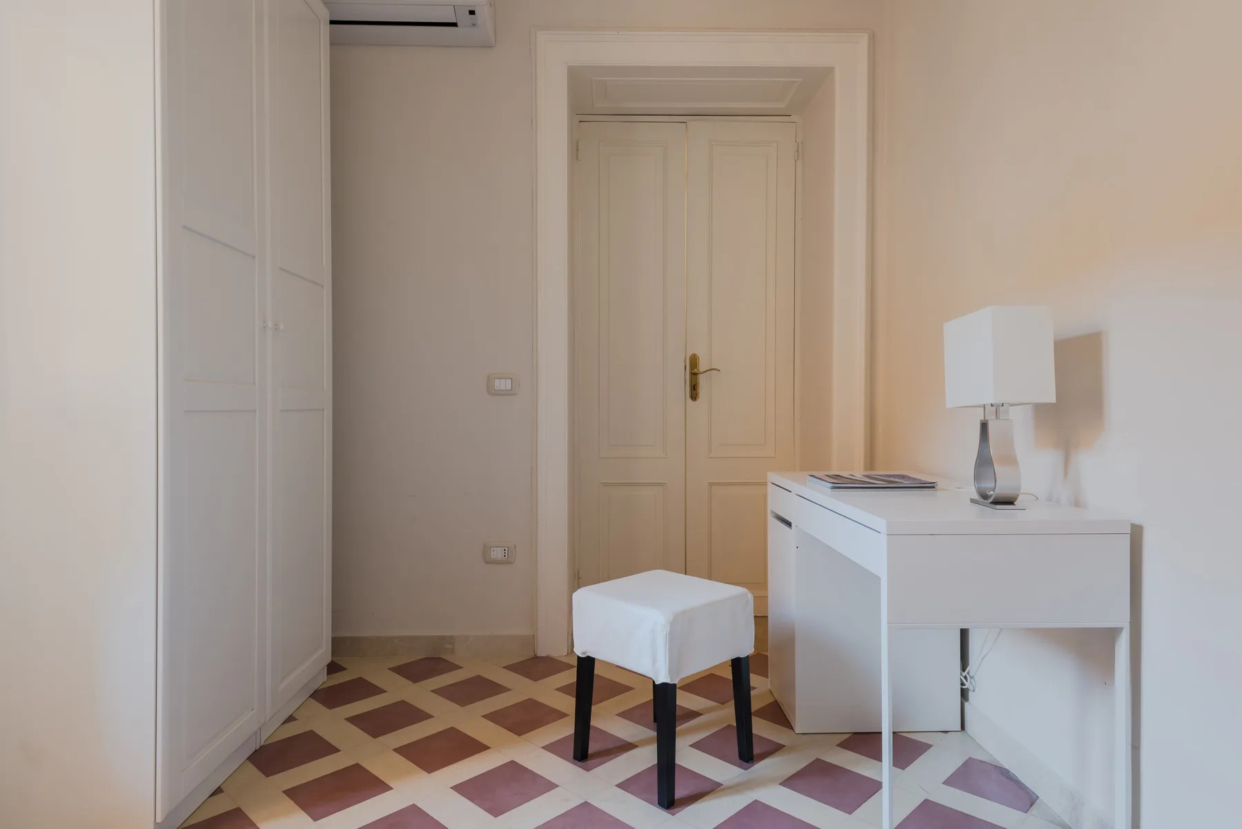 Zona de dormitorio con escritorio blanco, taburete y armario empotrado.