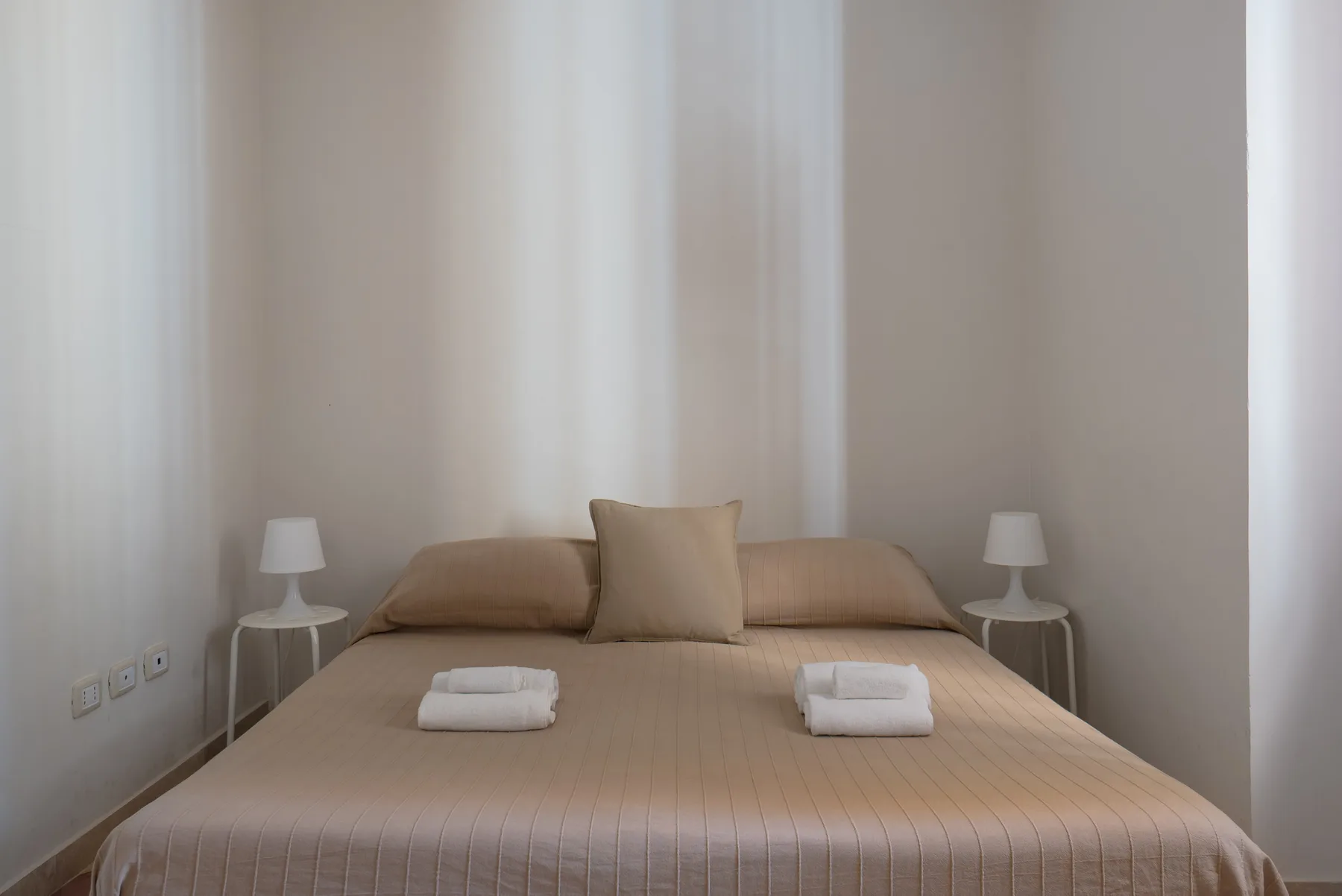 Un dormitorio con una cama bien hecha, almohadas y lámparas a ambos lados.