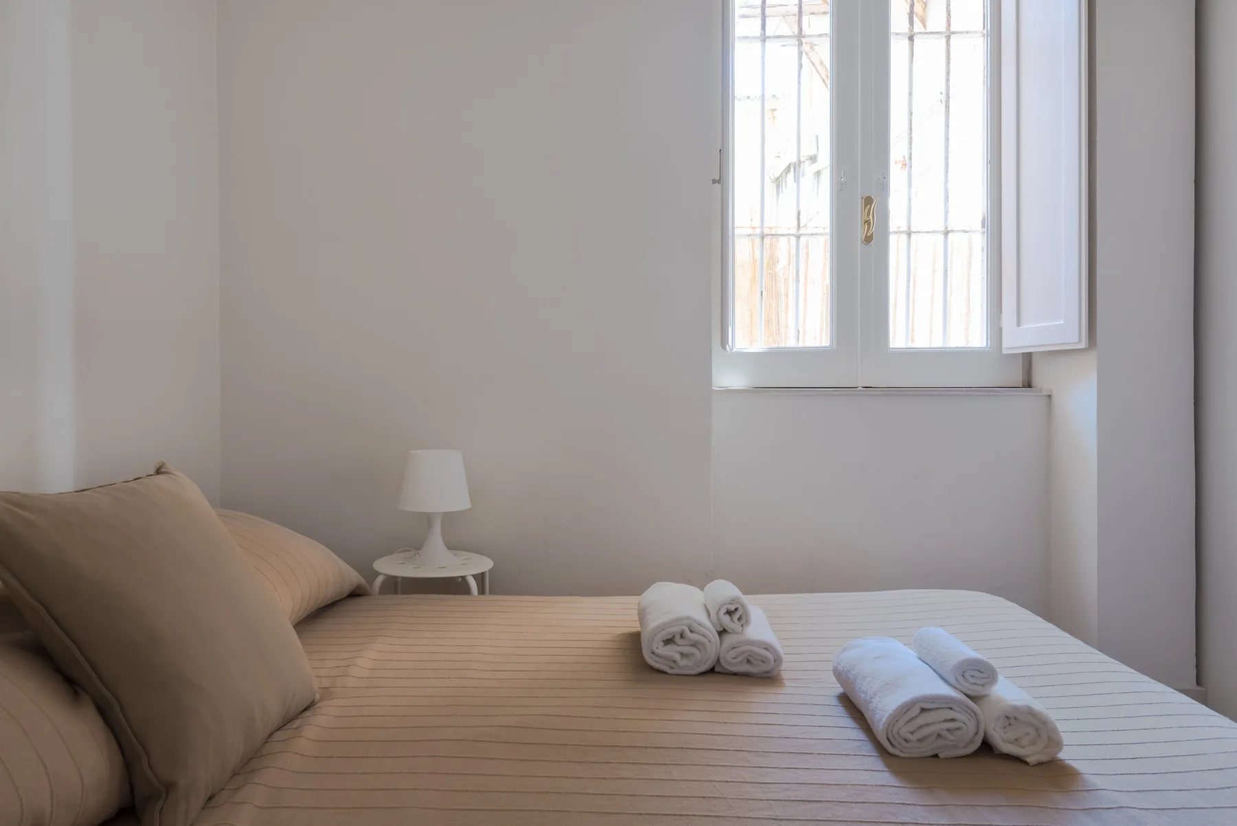 Un dormitorio con una cama ordenada y toallas dobladas bajo una ventana abierta.