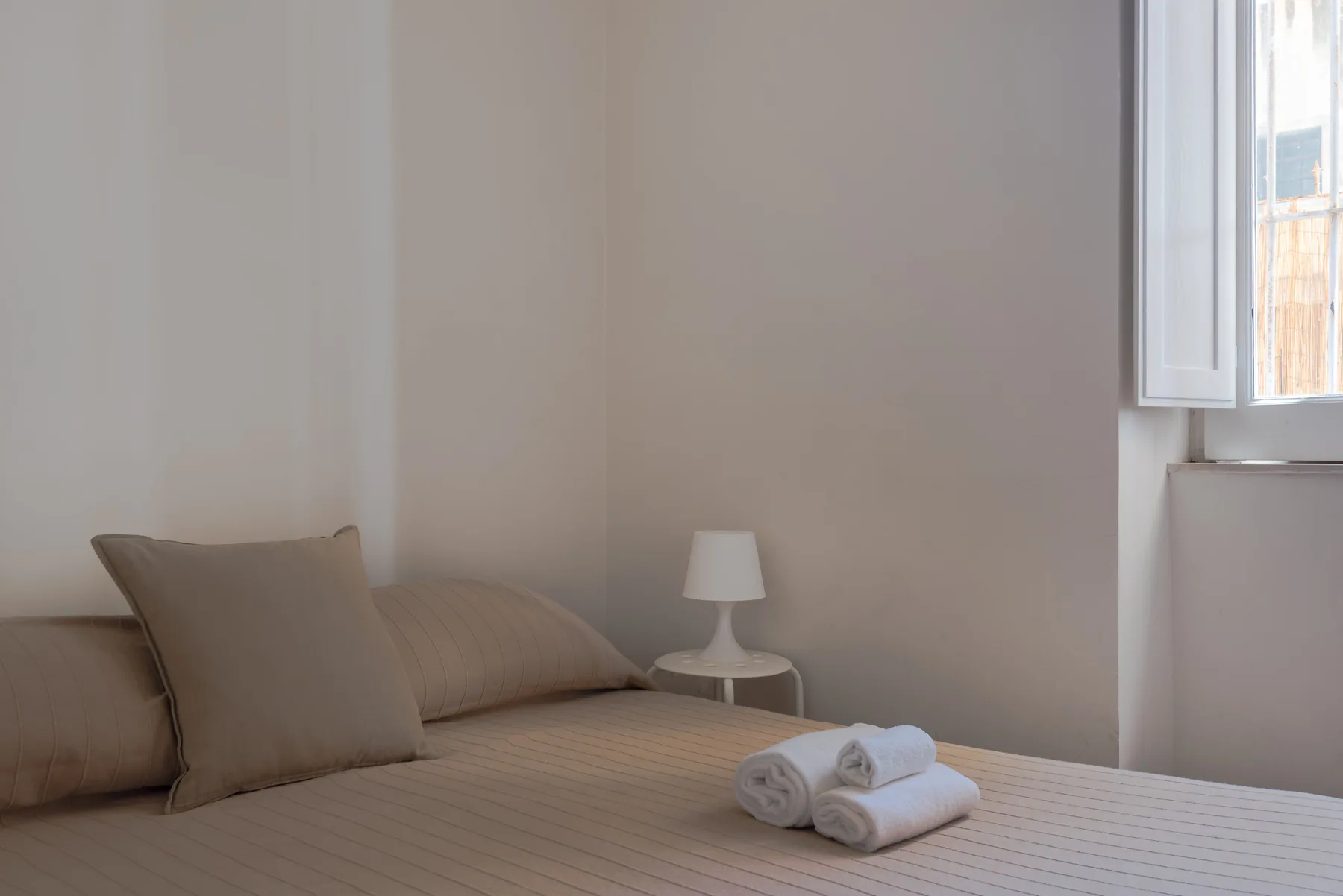 Un dormitorio con una cama, toallas dobladas y una pequeña lámpara de noche.