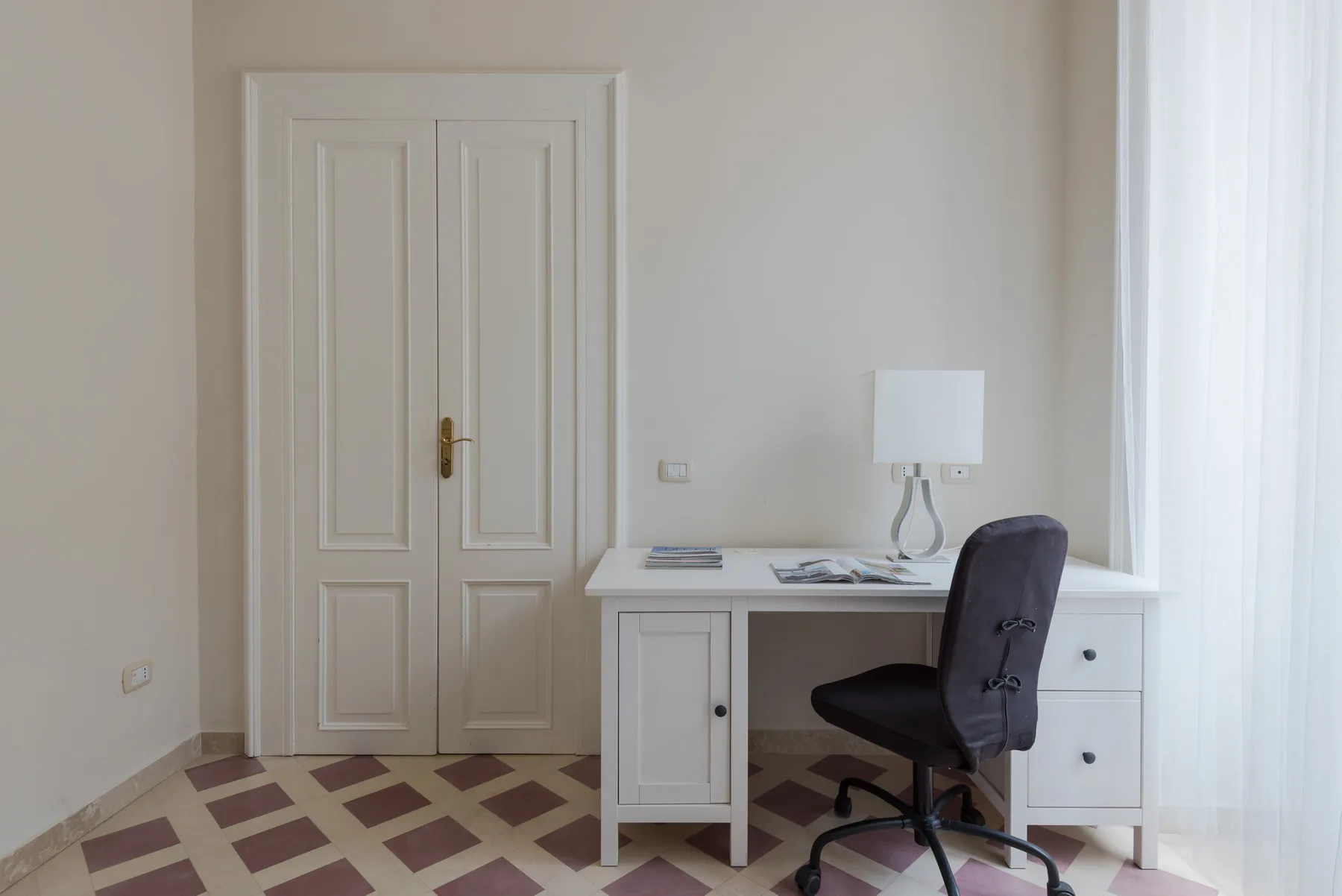Una habitación luminosa con escritorio, silla y puertas dobles con paneles.
