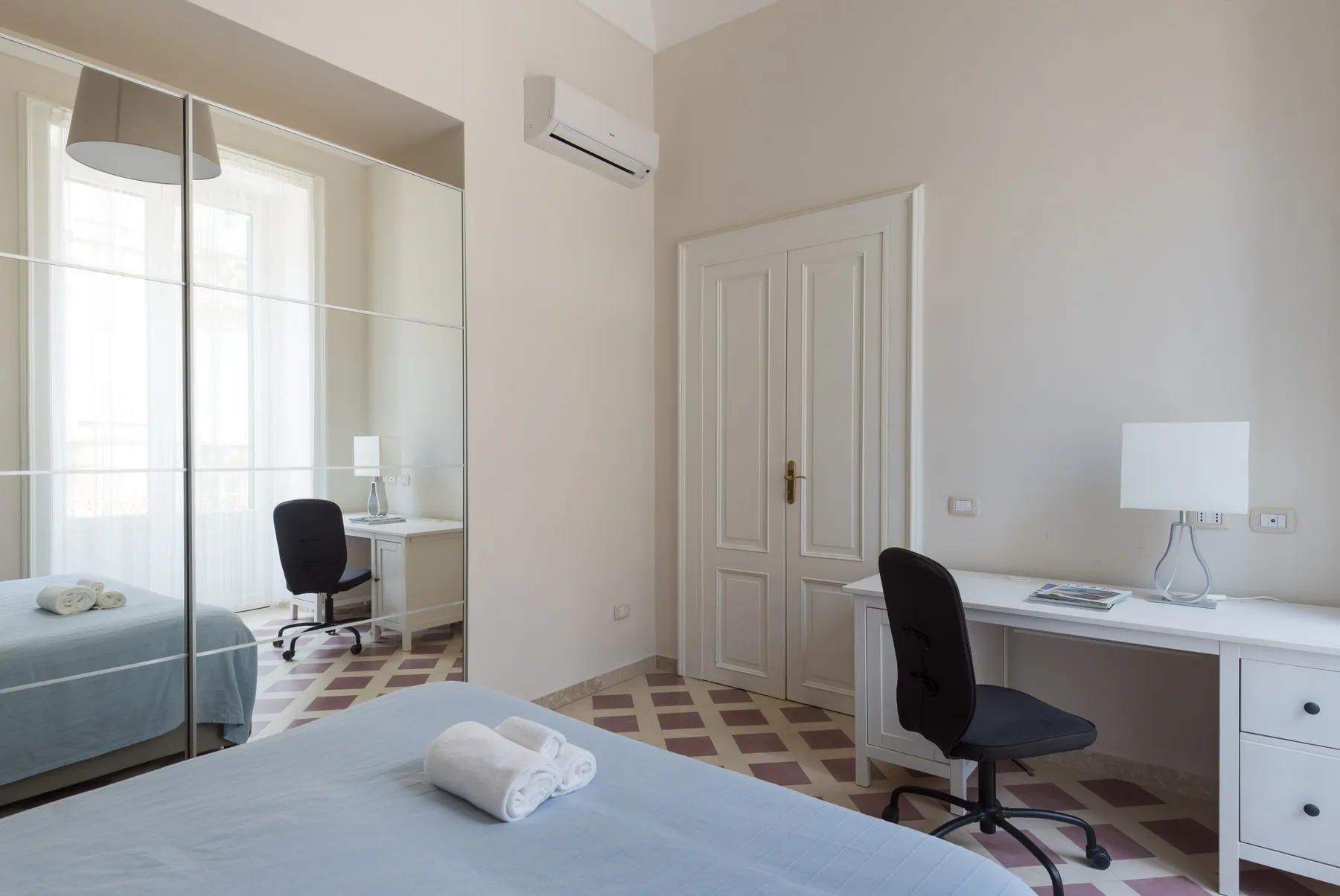 Un dormitorio con cama, armario con espejo y escritorio junto a la puerta.
