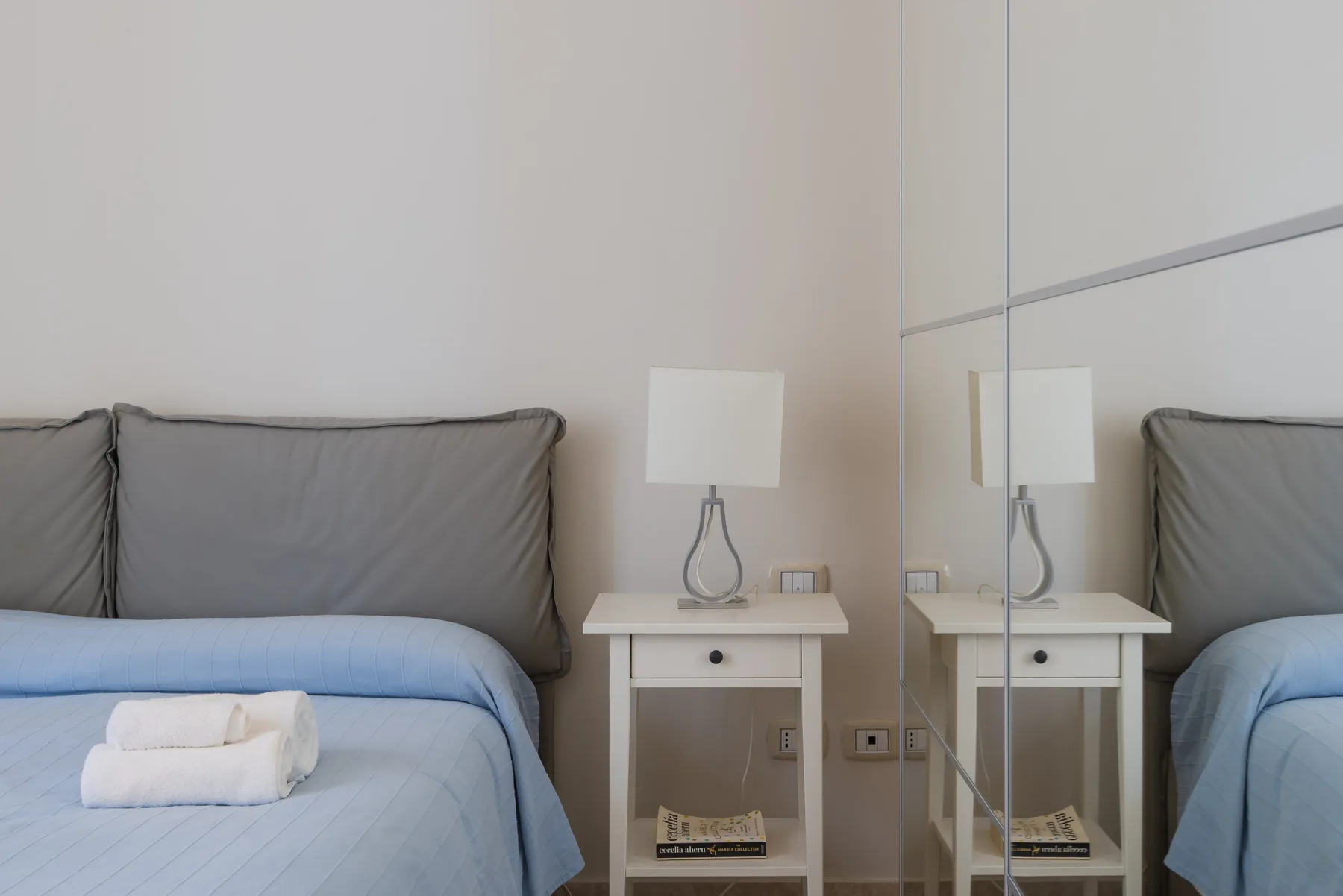 Un dormitorio con una cama tendida y una mesita de noche junto a un espejo.