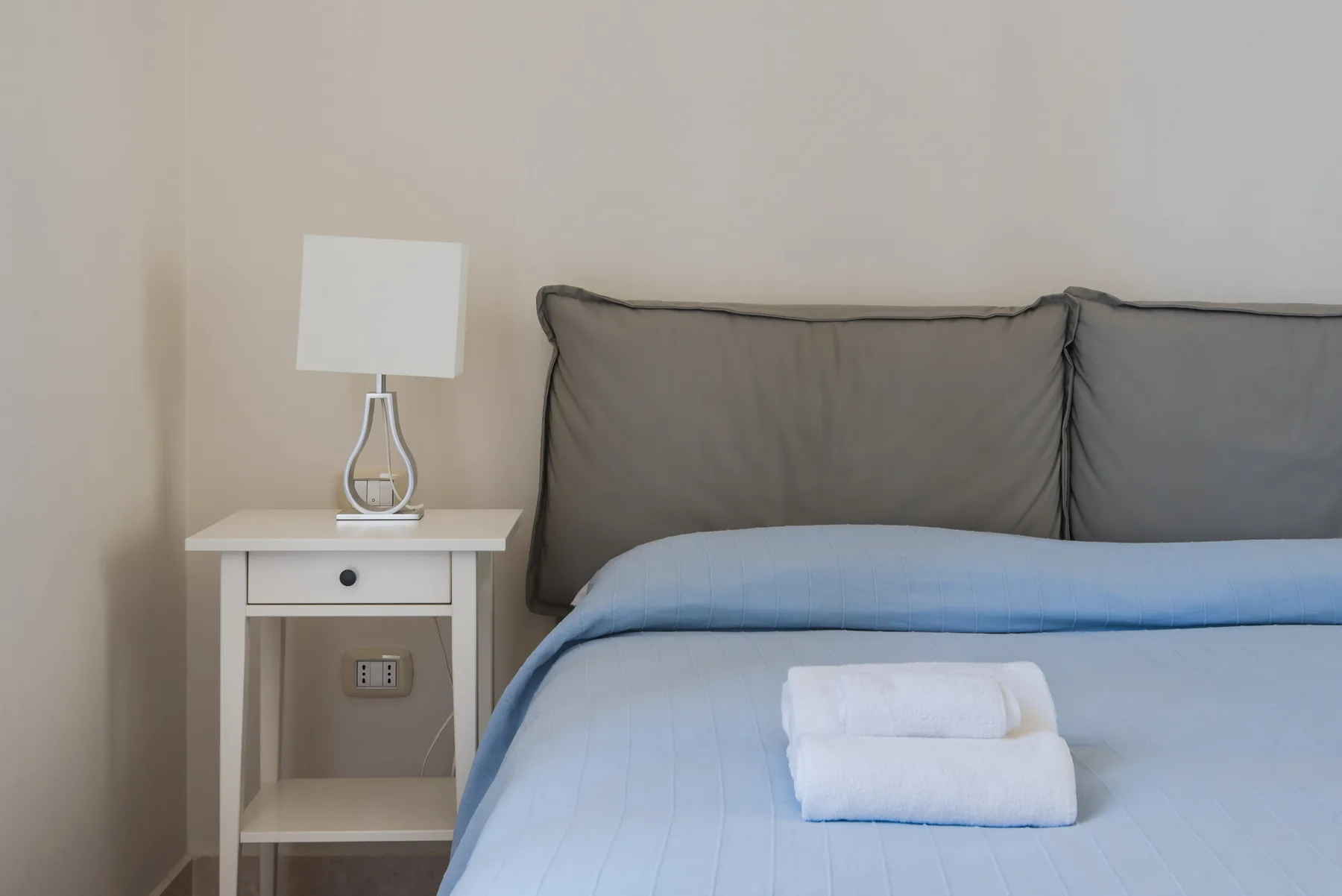 Una cama bien tendida con ropa de cama azul y una mesita de noche con lámpara.