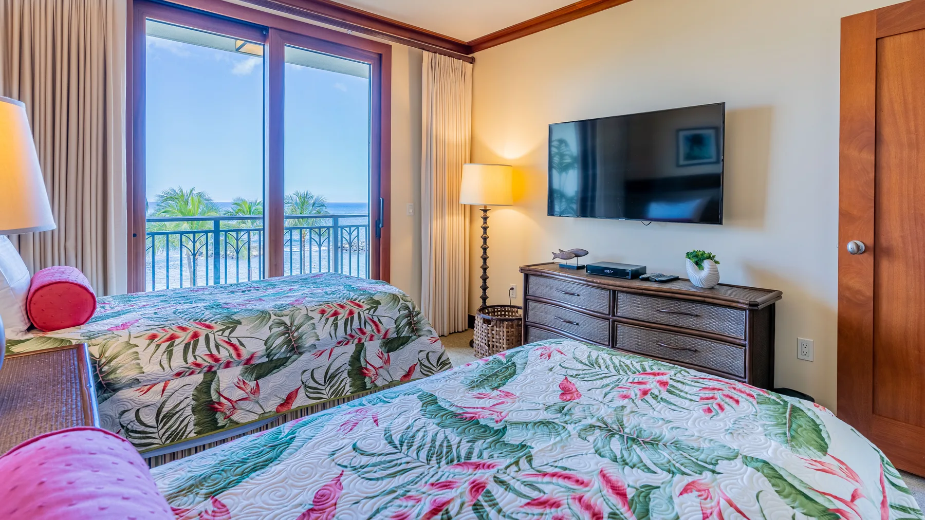 Un dormitorio con dos camas, ropa de cama floral y un televisor en la pared.