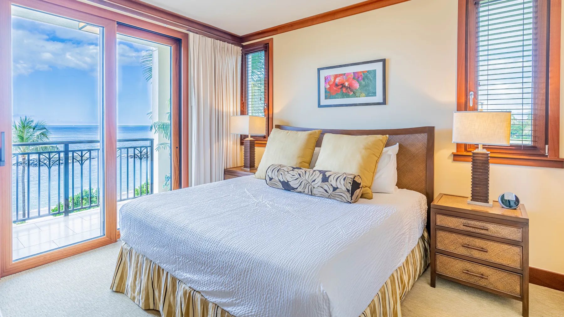 Un dormitorio con una cama bien tendida junto a grandes ventanas con vista al agua.