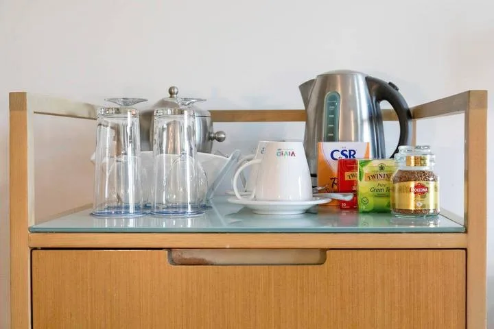 A refreshment station with a kettle, cups, and jars sits on a wooden cabinet.
