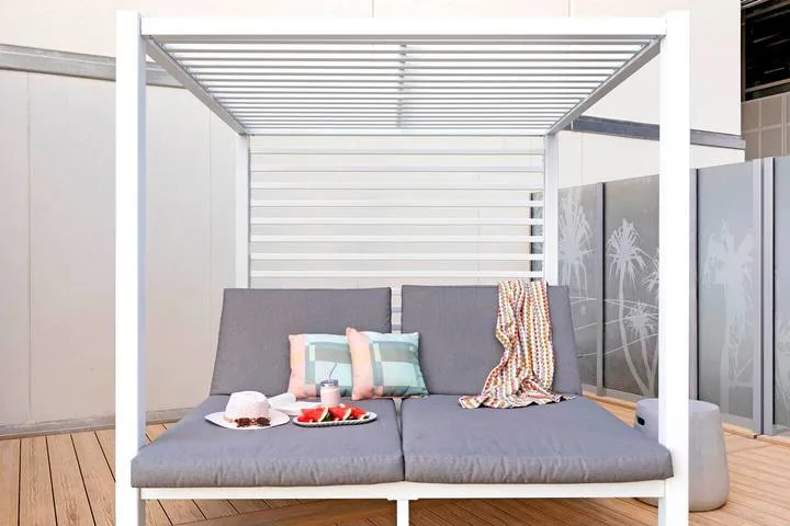 An outdoor daybed with cushions sits beneath a slatted canopy on a wooden deck.