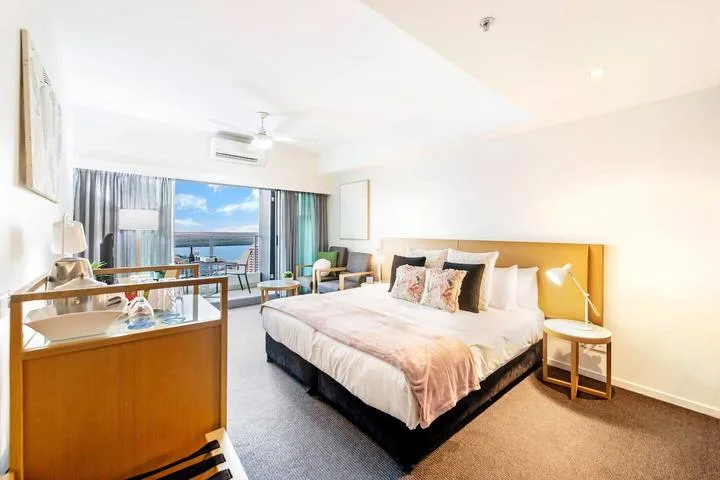 A bright bedroom with a large bed and seating beside a window.