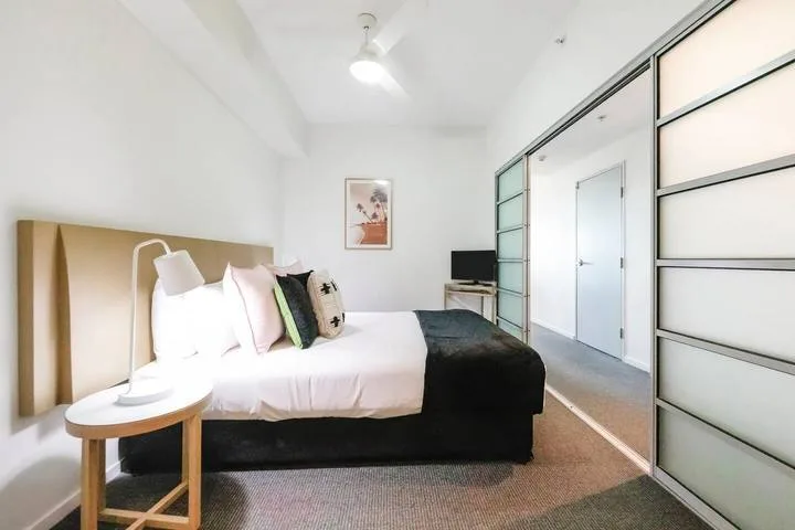 A bedroom with a bed, bedside table, and mirrored closet doors.