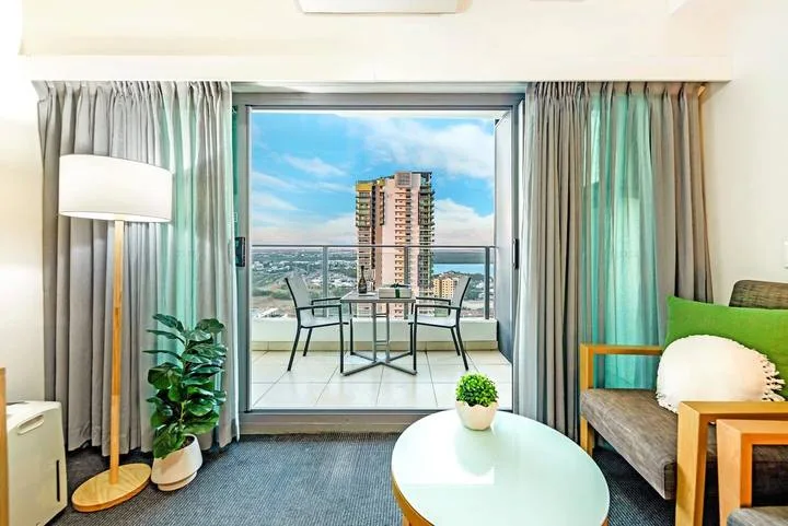 A bright living room opens onto a balcony with a small table and chairs.