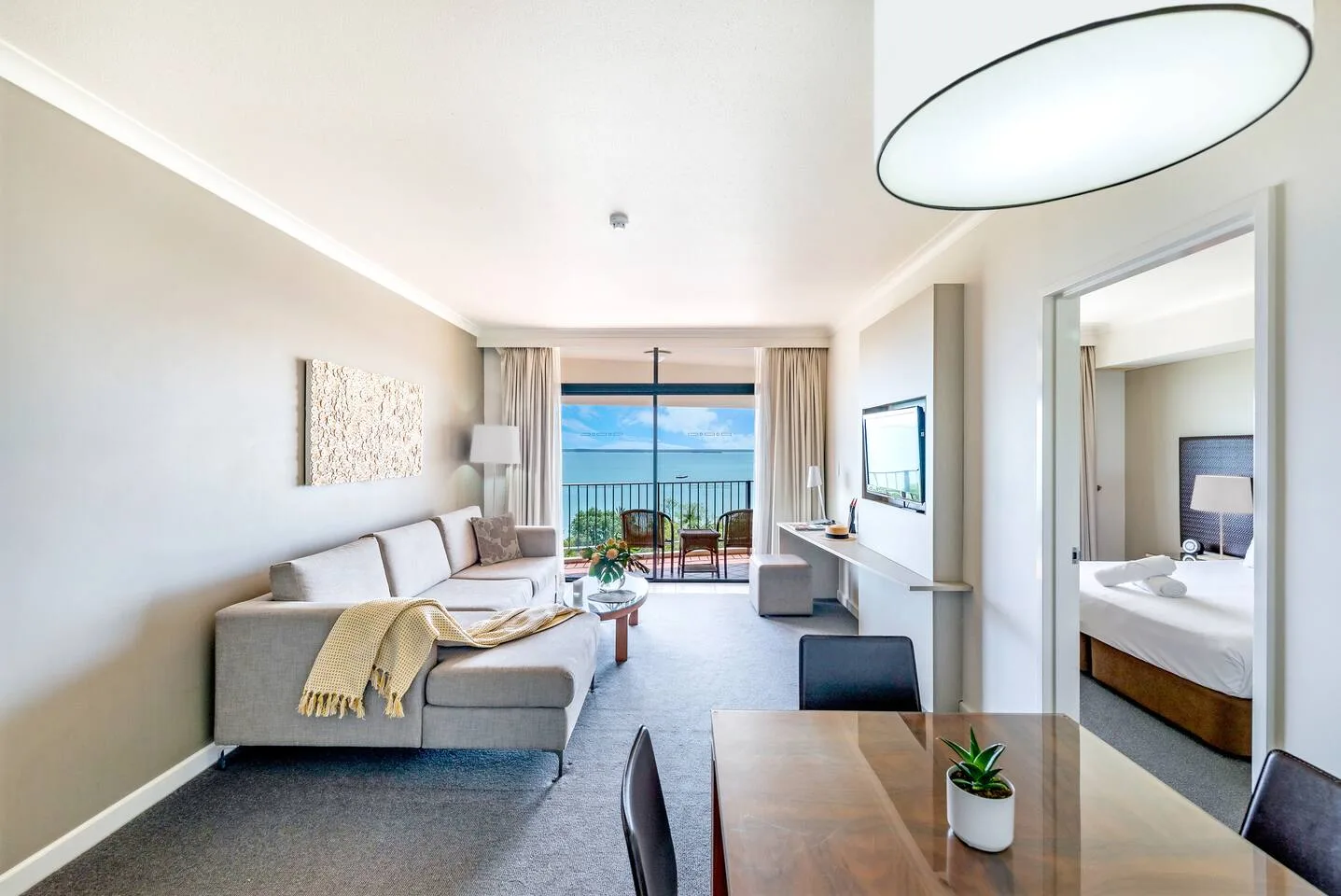 A living room with seating and a dining table faces a balcony with glass doors.
