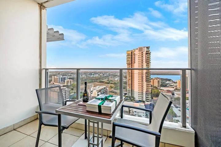 A balcony seating area overlooks nearby buildings beneath a blue sky.