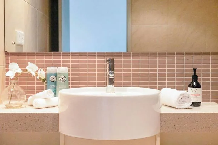 A bathroom vanity features a white vessel sink against a pink tiled backsplash.