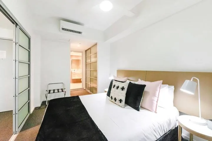 A bedroom with a white bed, black throw, and bedside lamp.