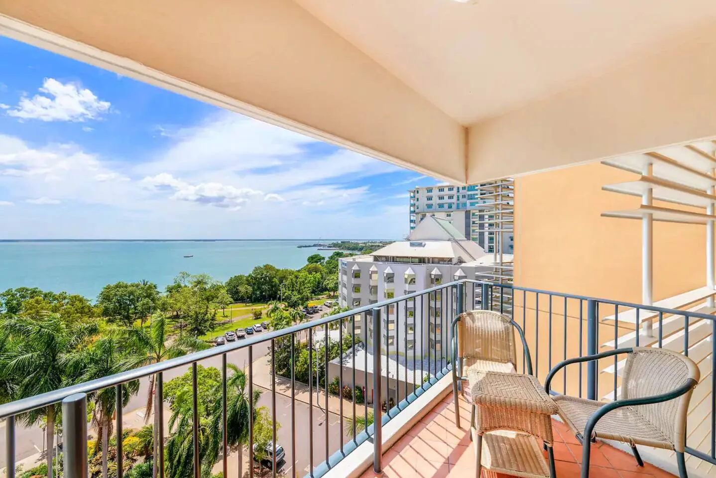 A balcony with seating overlooks trees, nearby buildings, and a body of water.
