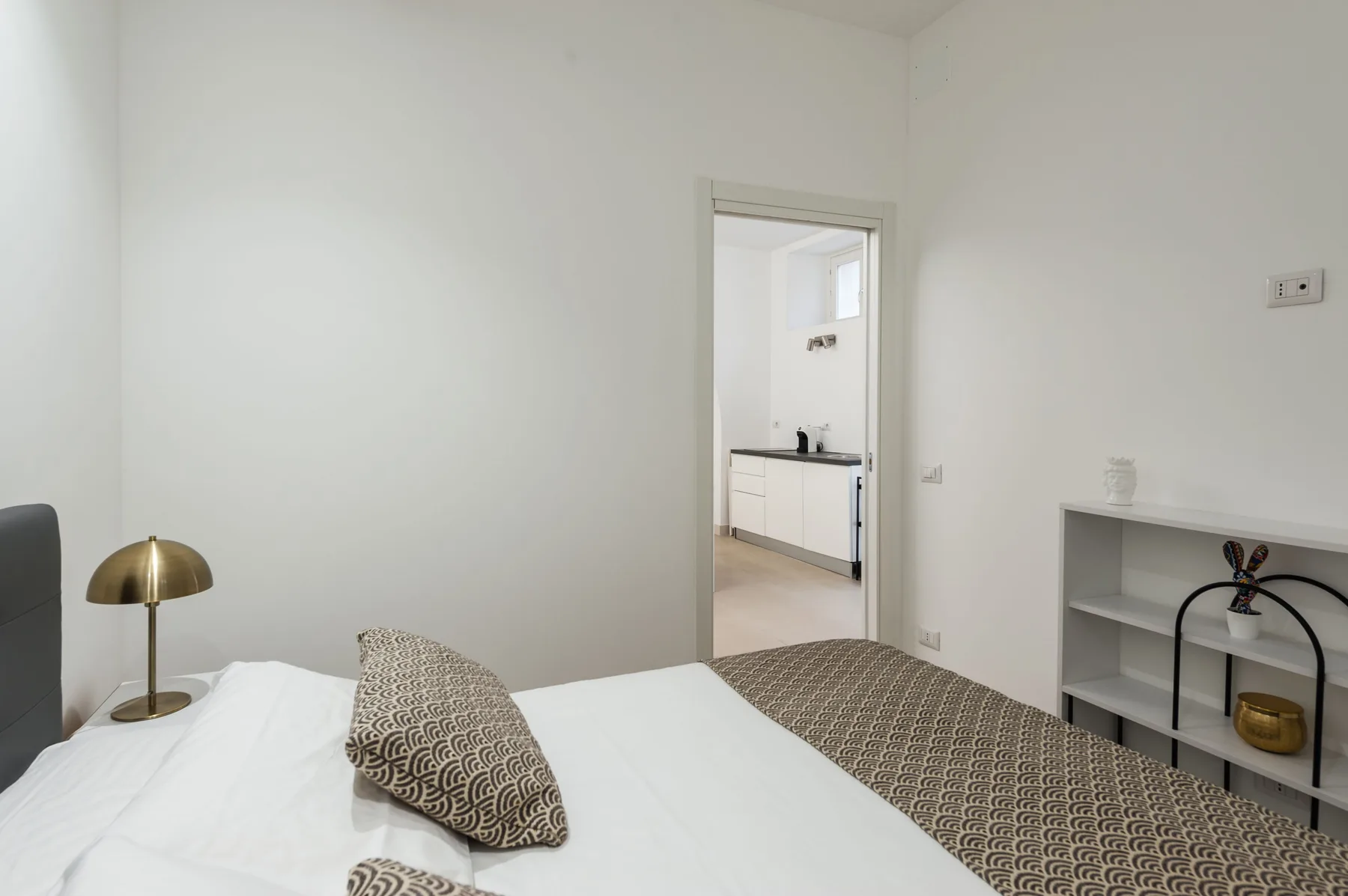 Un dormitorio con ropa de cama blanca y una vista al baño por una puerta abierta.