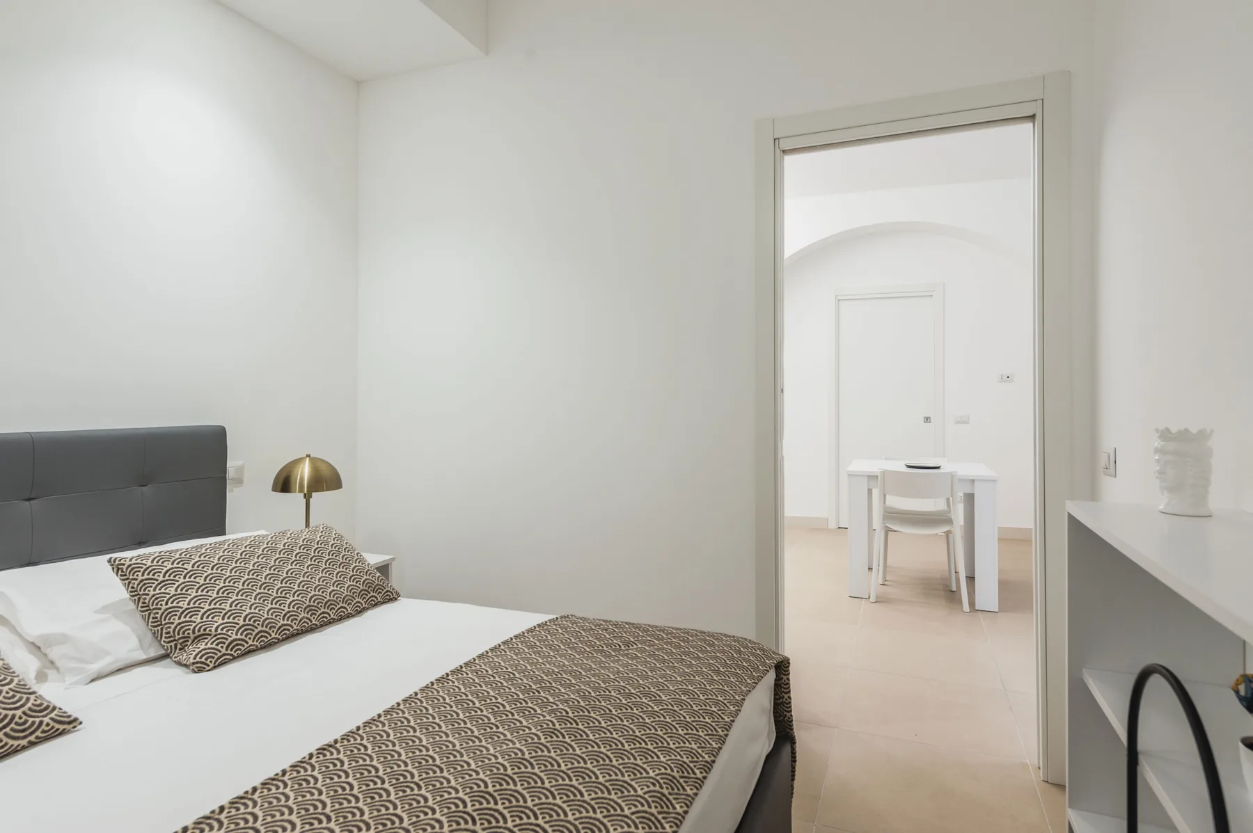 Un dormitorio con una cama junto a una puerta abierta hacia un comedor.