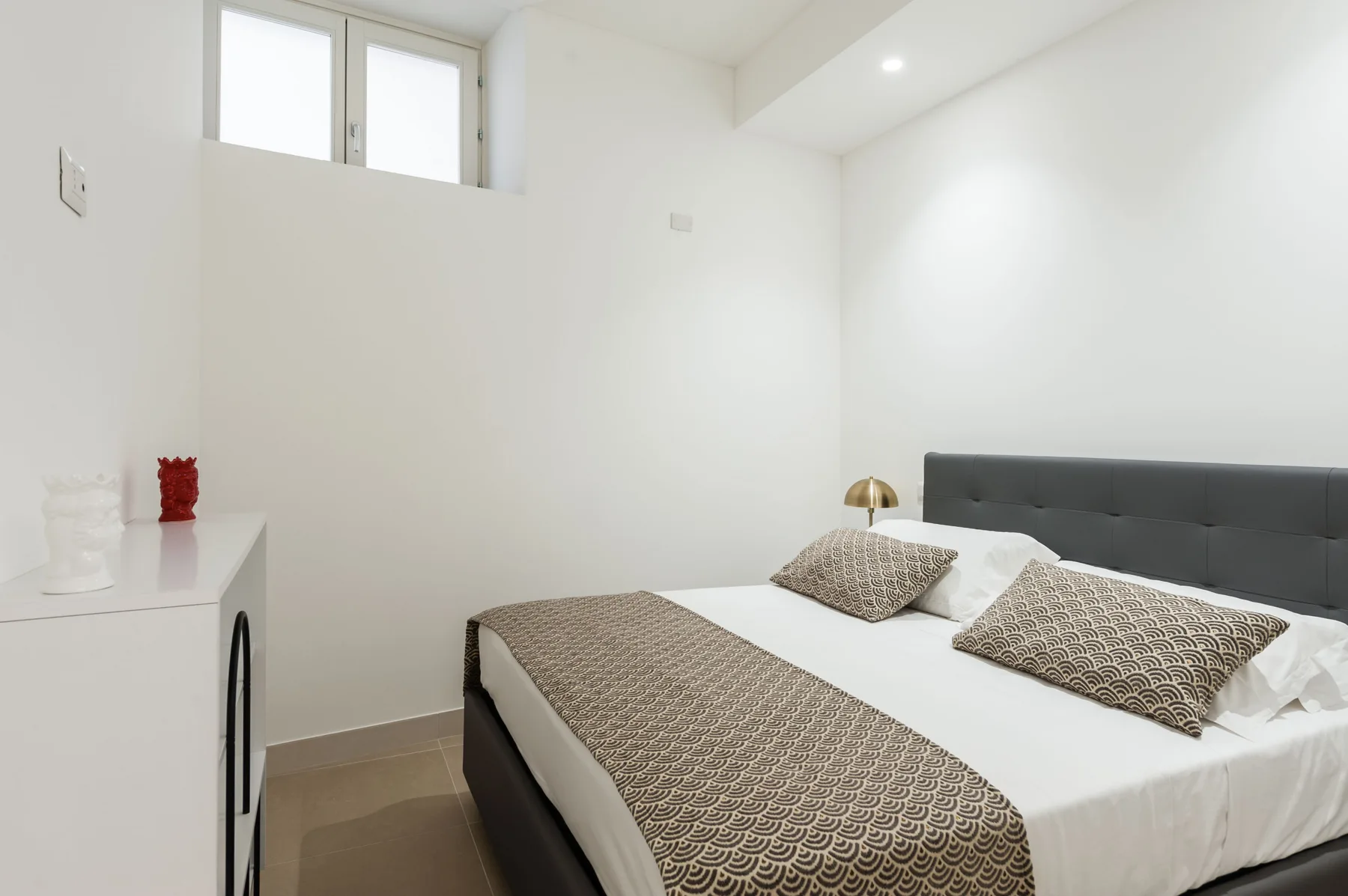 Un dormitorio luminoso con una cama vestida con ropa blanca y ropa de cama estampada.