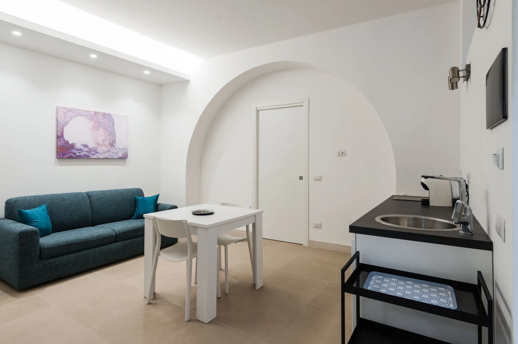 Una luminosa sala de estar con asientos, una mesa pequeña y una cocina compacta.