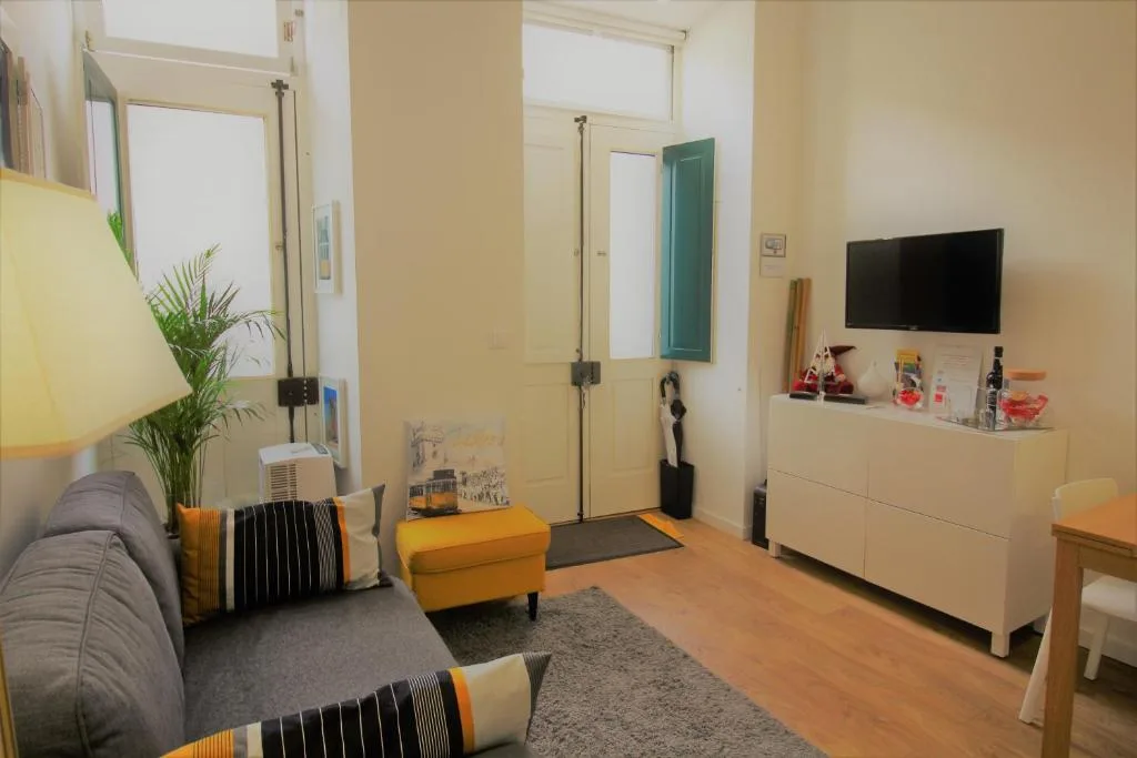 Sala de estar con asientos, un televisor y ventanas altas.