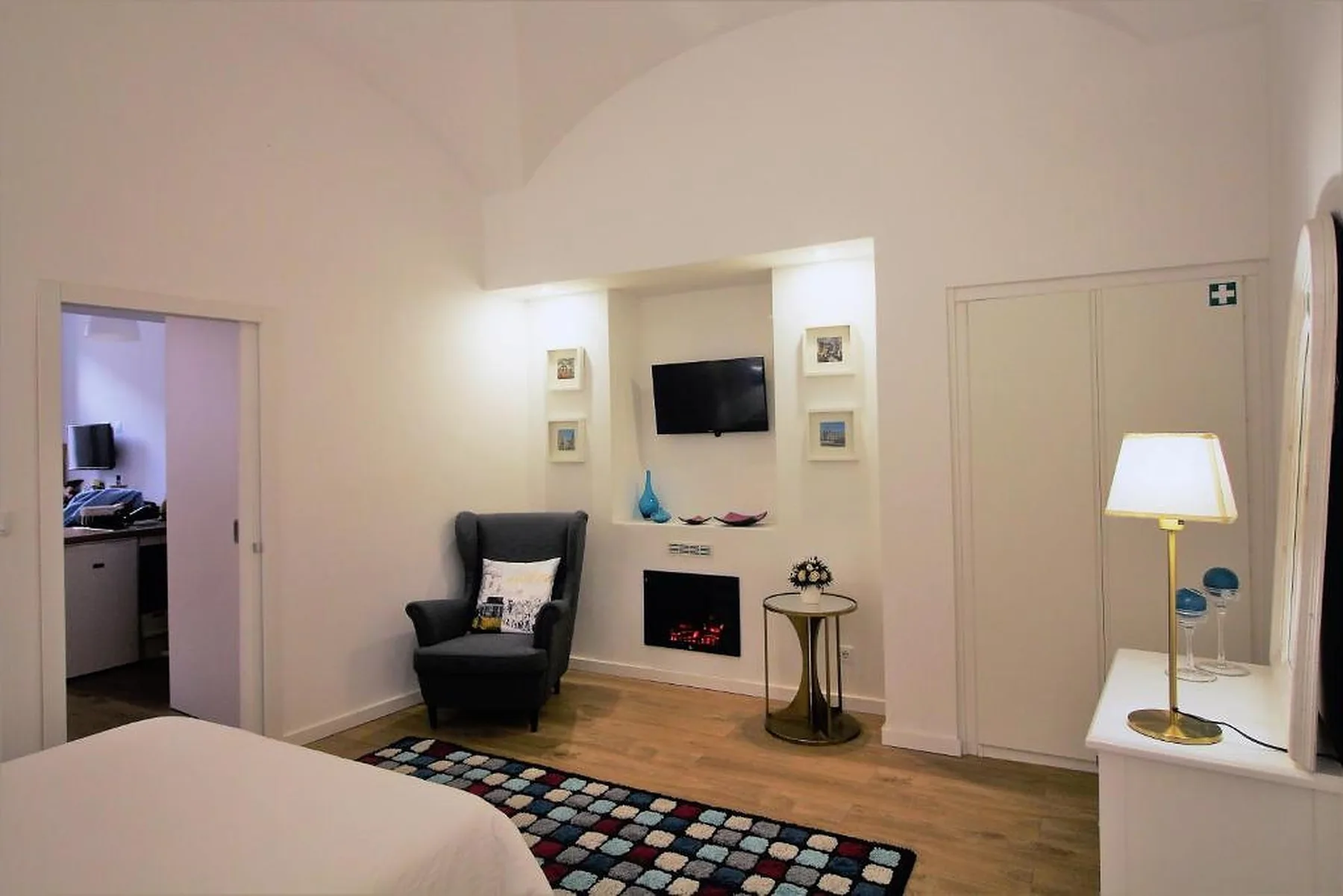 A bedroom with a bed, an armchair, and a television above the fireplace.