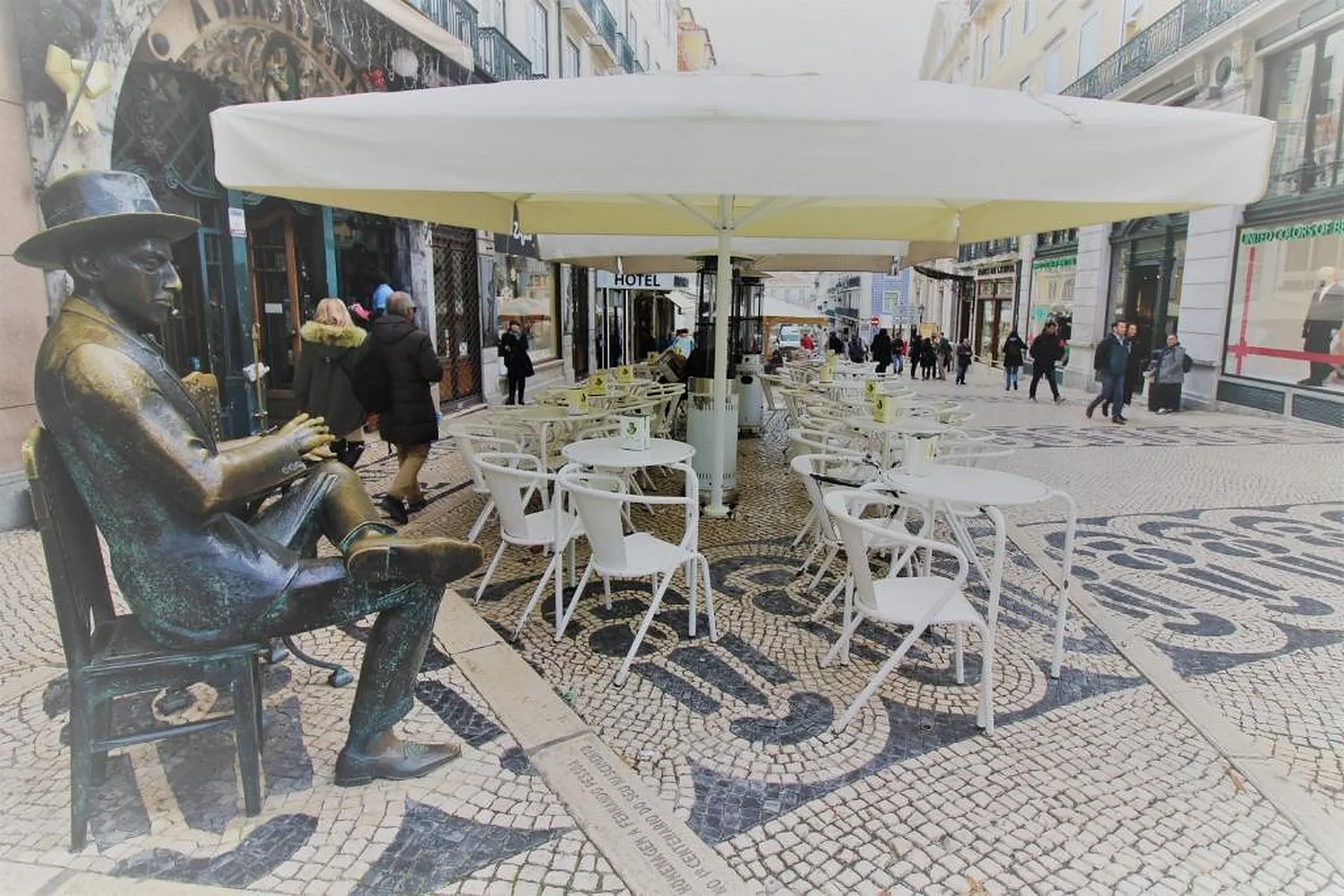 Outdoor café seating beneath a canopy on a pedestrian street with patterned paving.