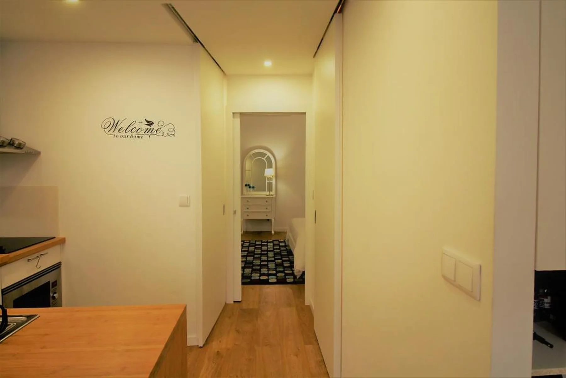 A narrow apartment hallway leads to a bathroom, with part of a kitchen visible.