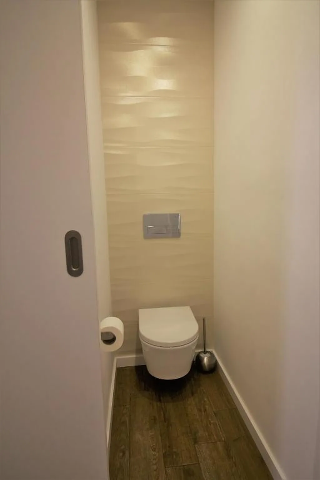 A compact bathroom with a wall-mounted toilet and a flush plate.
