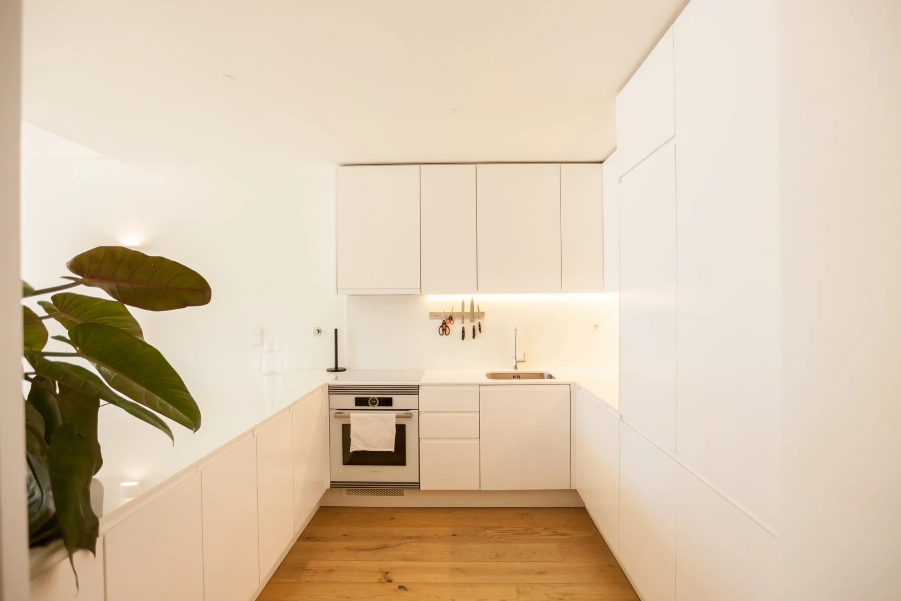 Una cocina moderna y luminosa con armarios blancos y suelo de madera.