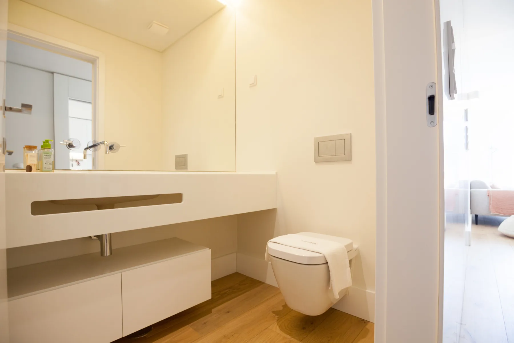 Baño con una amplia encimera de lavabo y un inodoro junto a una puerta luminosa.