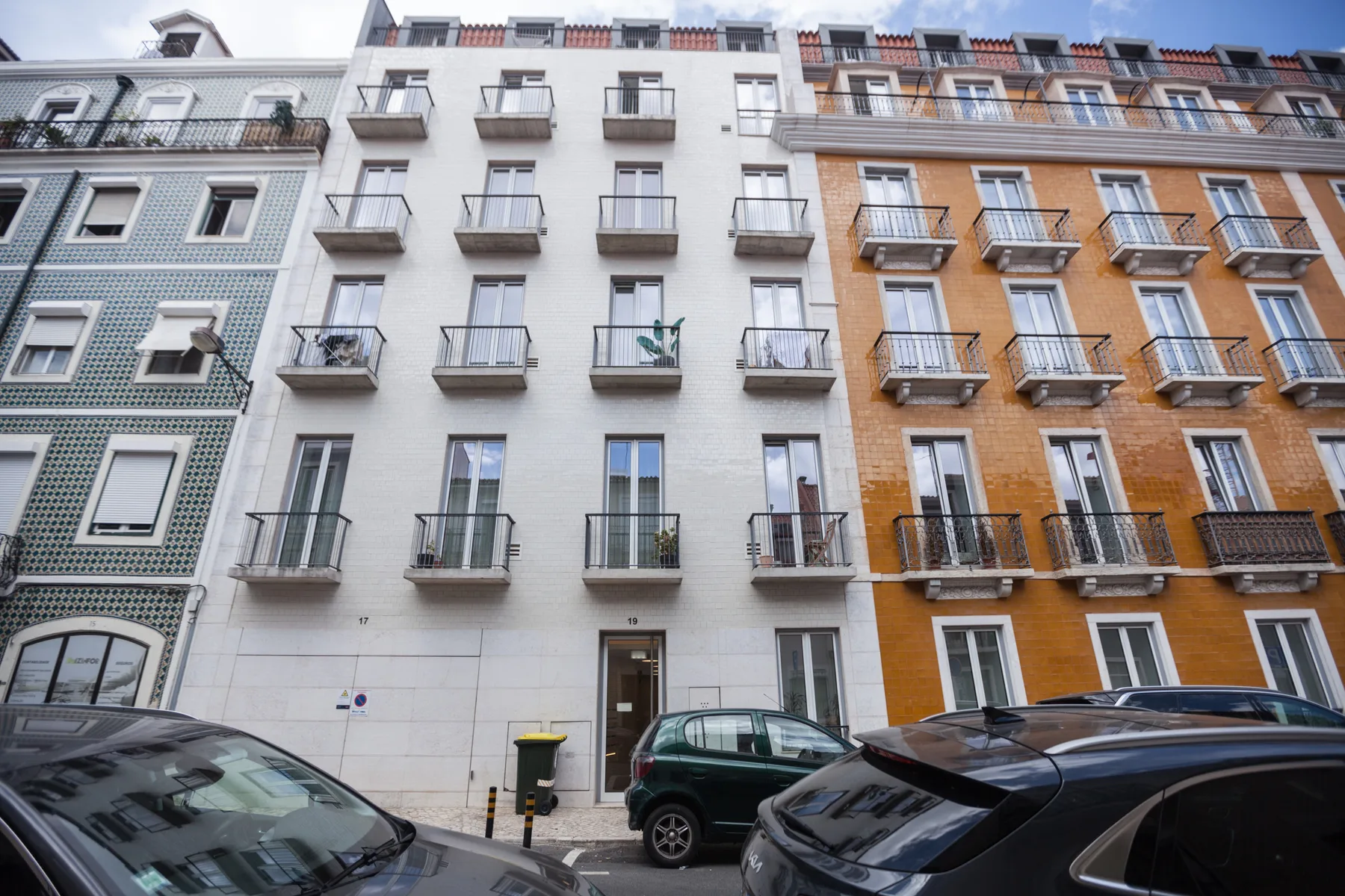 Una fila de edificios de apartamentos con balcones da a una calle con coches estacionados.