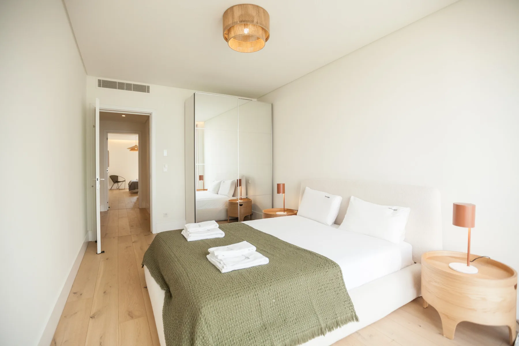 Un dormitorio luminoso con ropa de cama blanca y una manta verde sobre la cama.