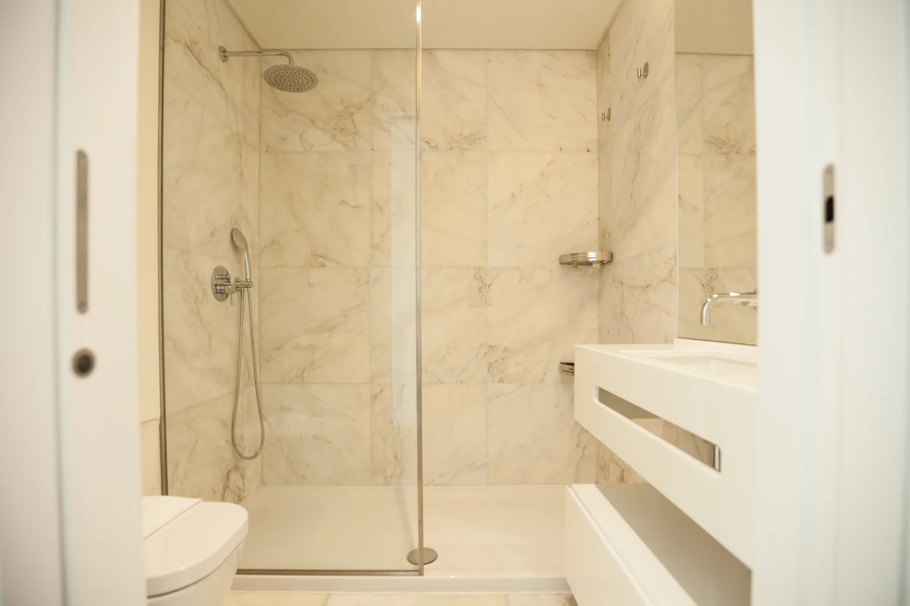 Un baño luminoso con ducha de vidrio y un lavabo suspendido.