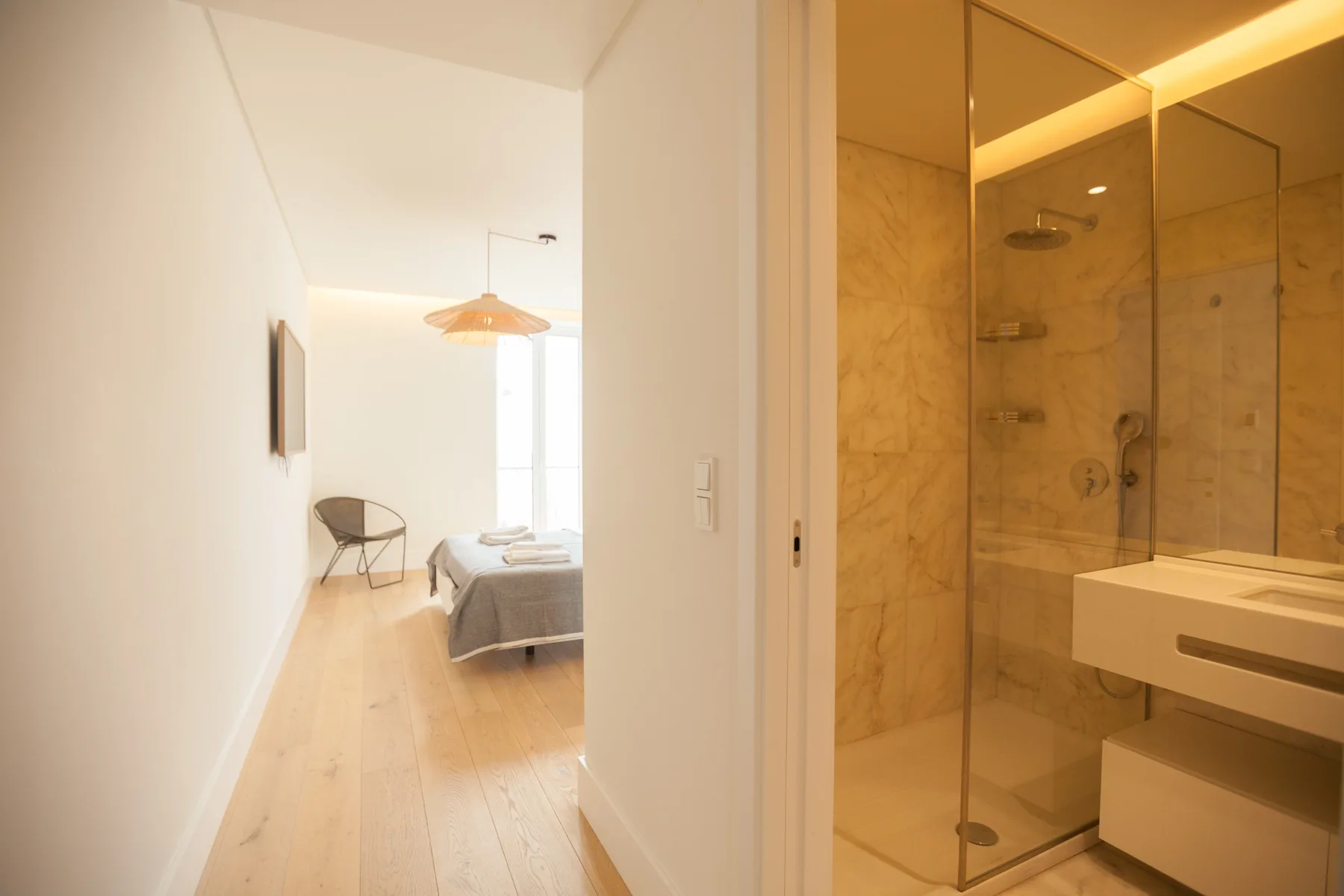 Un pasillo conduce a un dormitorio, junto a una ducha acristalada y el lavabo del baño.