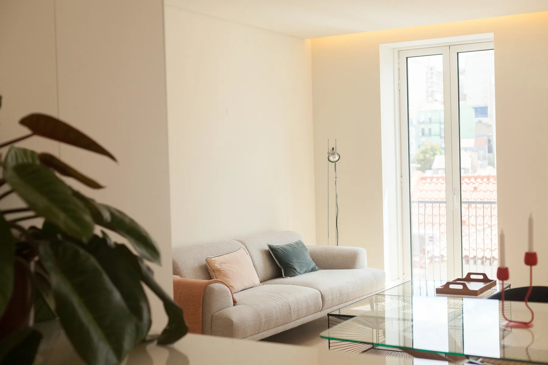Un salón luminoso con un sofá y una mesa de centro de cristal junto a ventanas altas.
