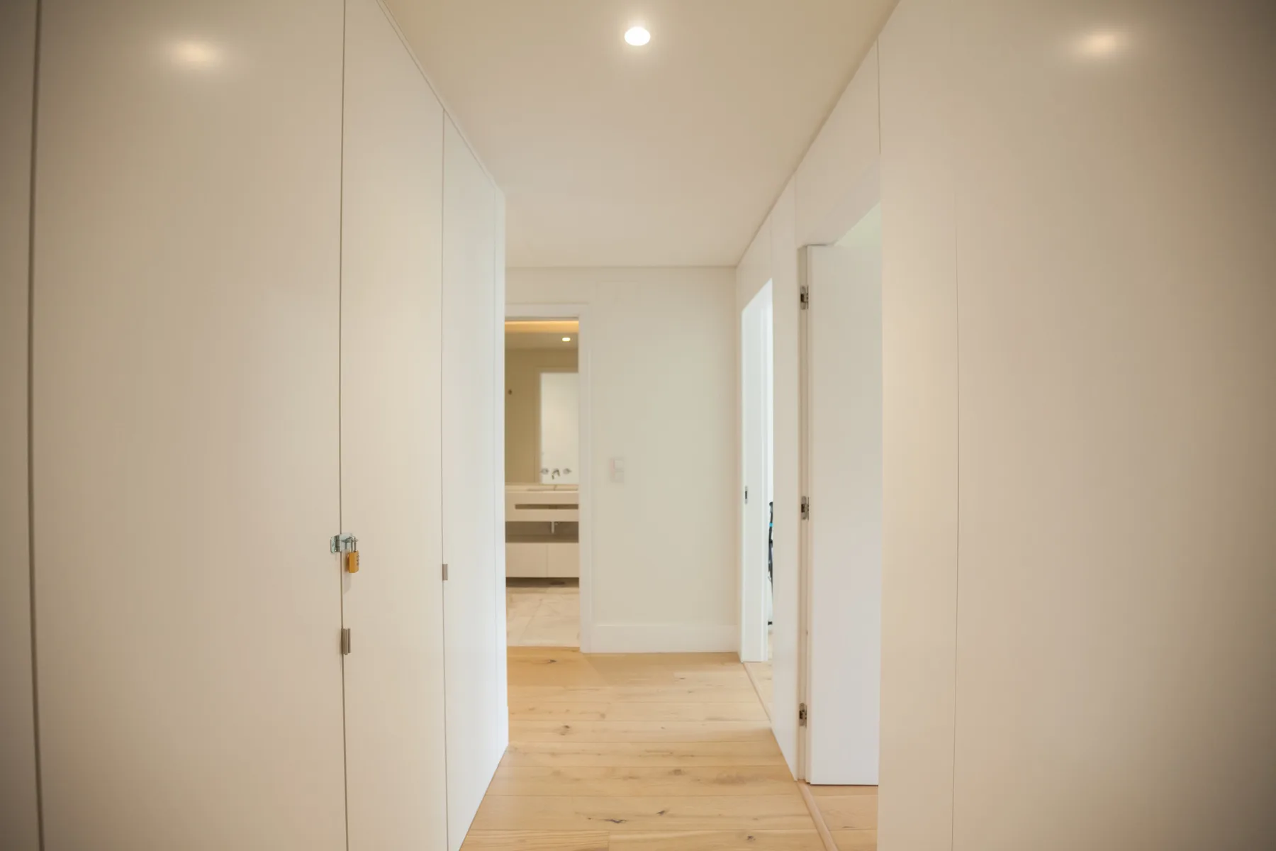 Un pasillo luminoso con puertas blancas y suelo de madera clara.