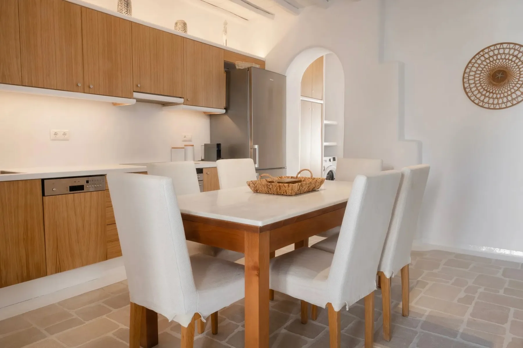 Comedor con una mesa de madera y asientos blancos junto a la cocina.