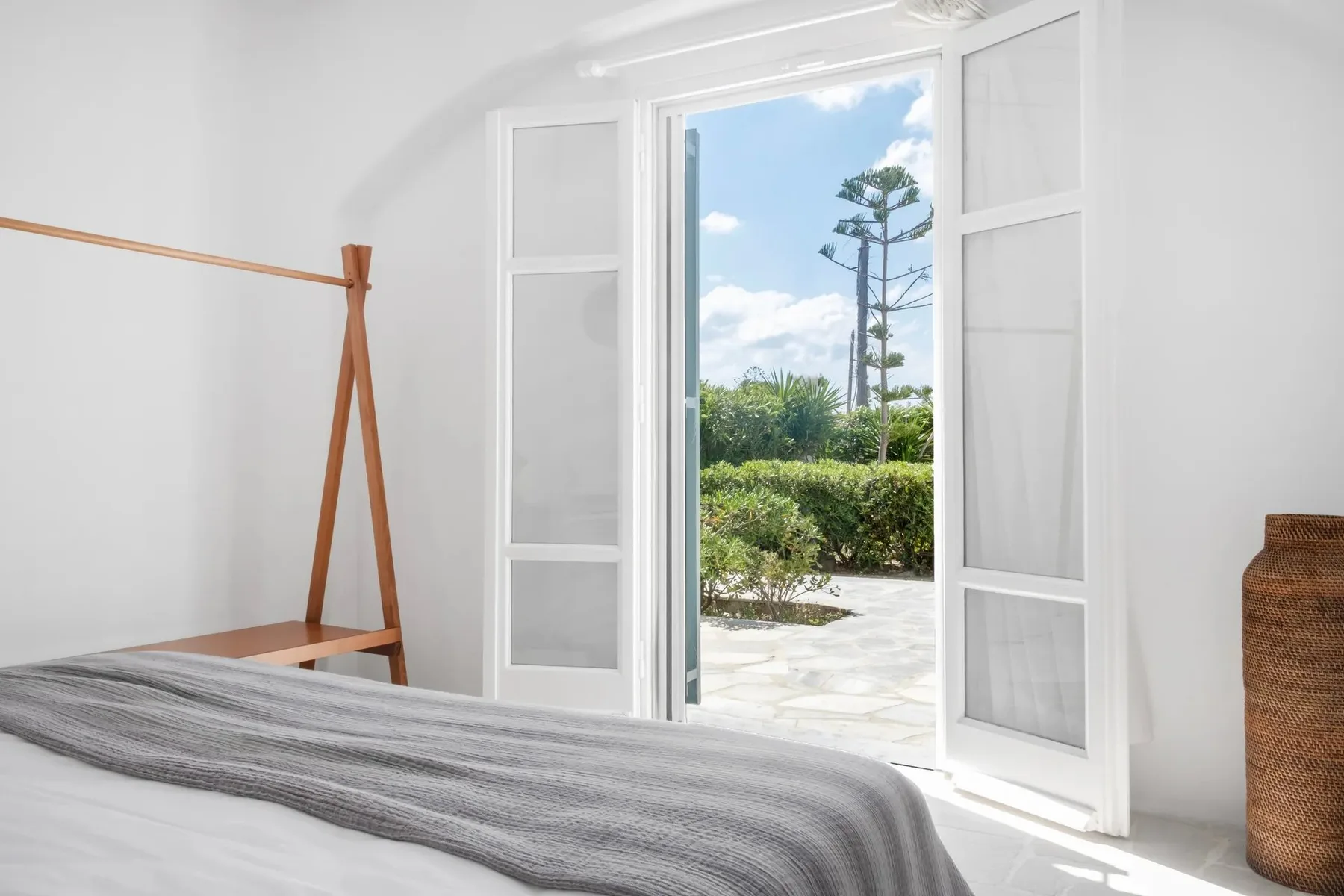Un dormitorio luminoso da a un jardín a través de puertas de vidrio abiertas.