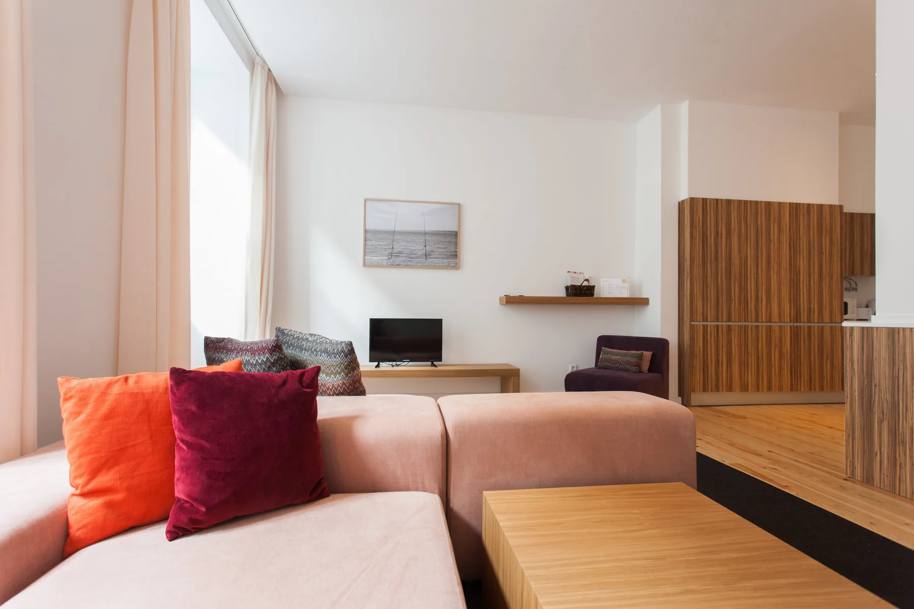 Una sala de estar luminosa con asientos rosas, una mesa de madera y un televisor.
