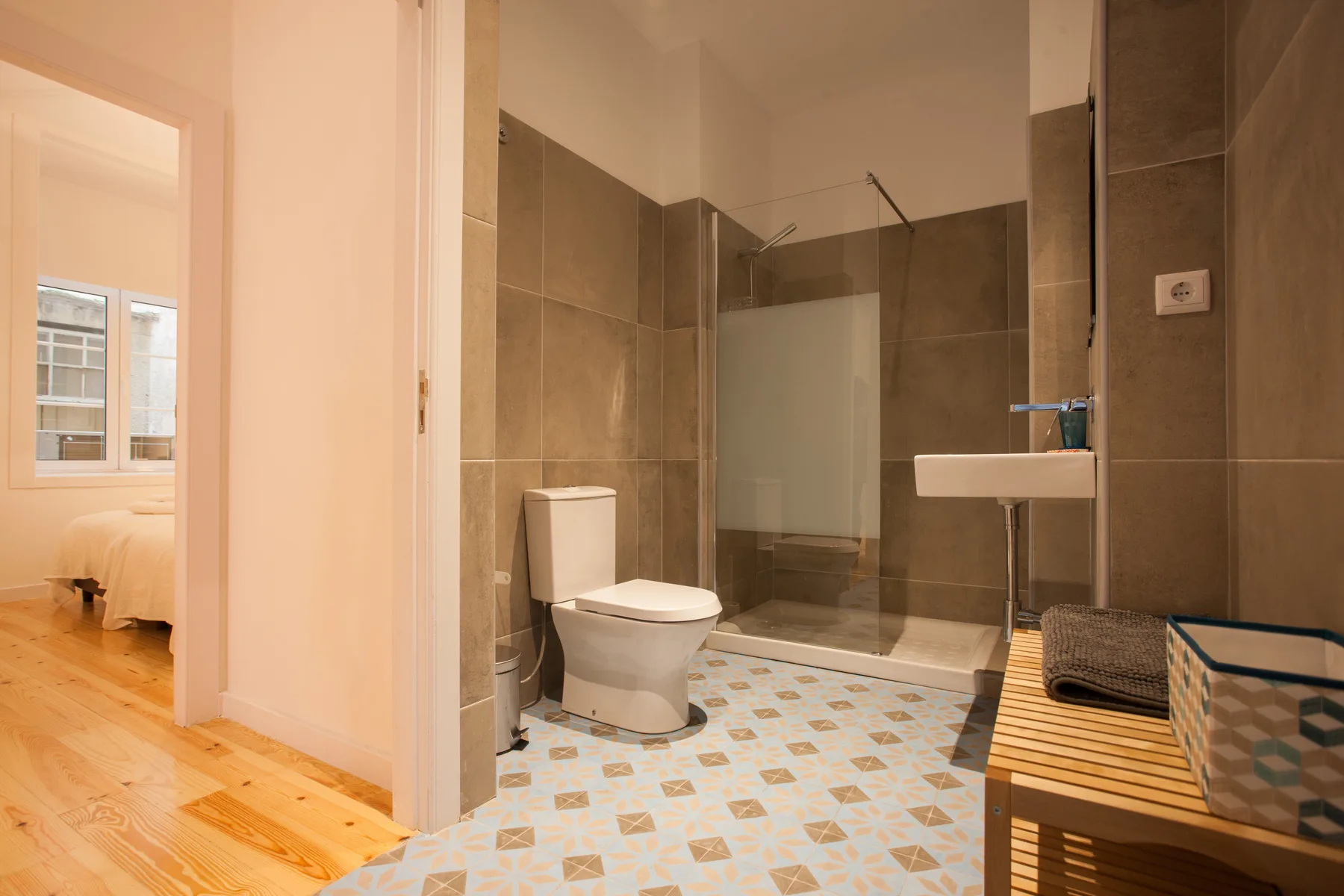 Un baño con inodoro, lavabo y ducha de vidrio junto a un dormitorio.