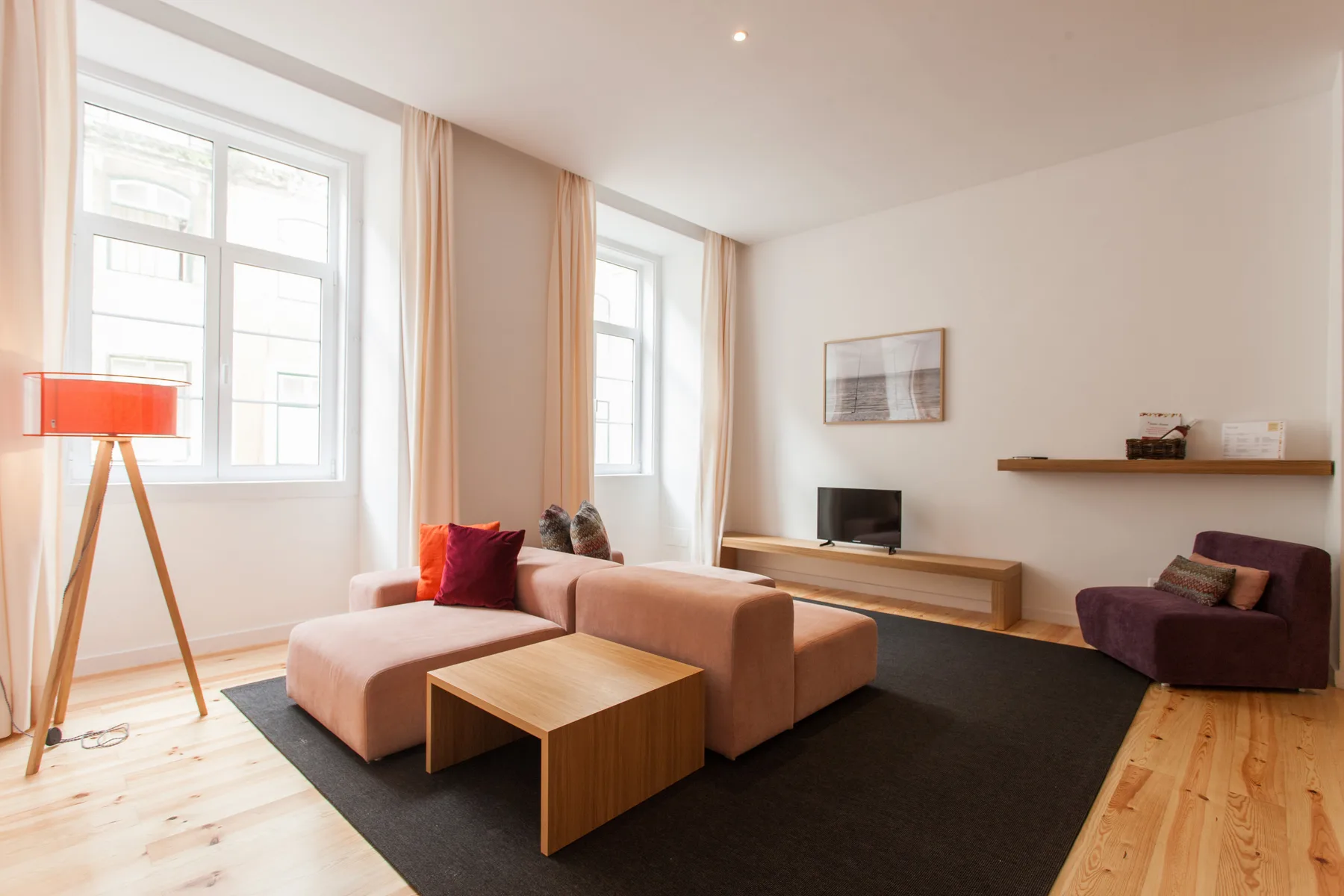 Una sala luminosa con asientos, un televisor y ventanas grandes.