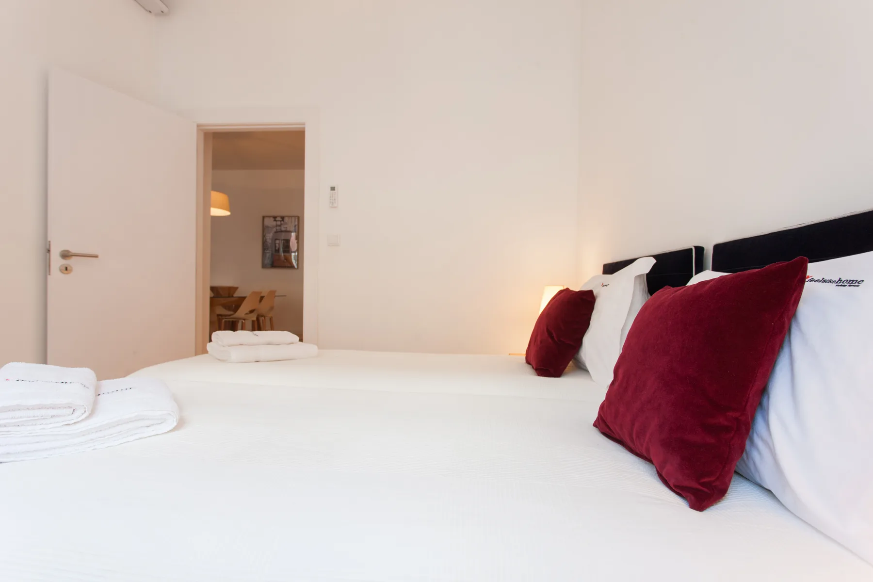 Un dormitorio con una cama blanca y cojines rojos junto a una puerta abierta.