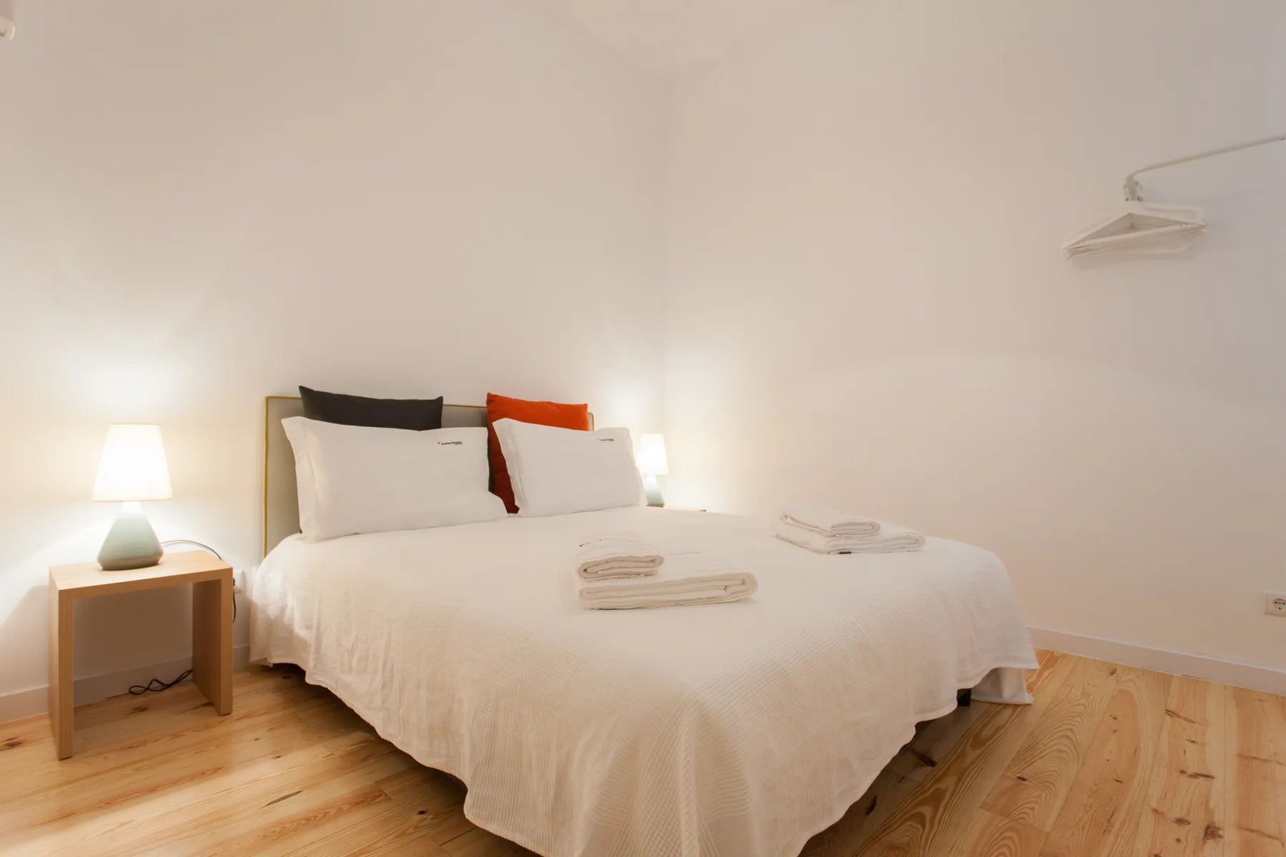 Un dormitorio luminoso con una cama, una mesita de noche y suelo de madera.