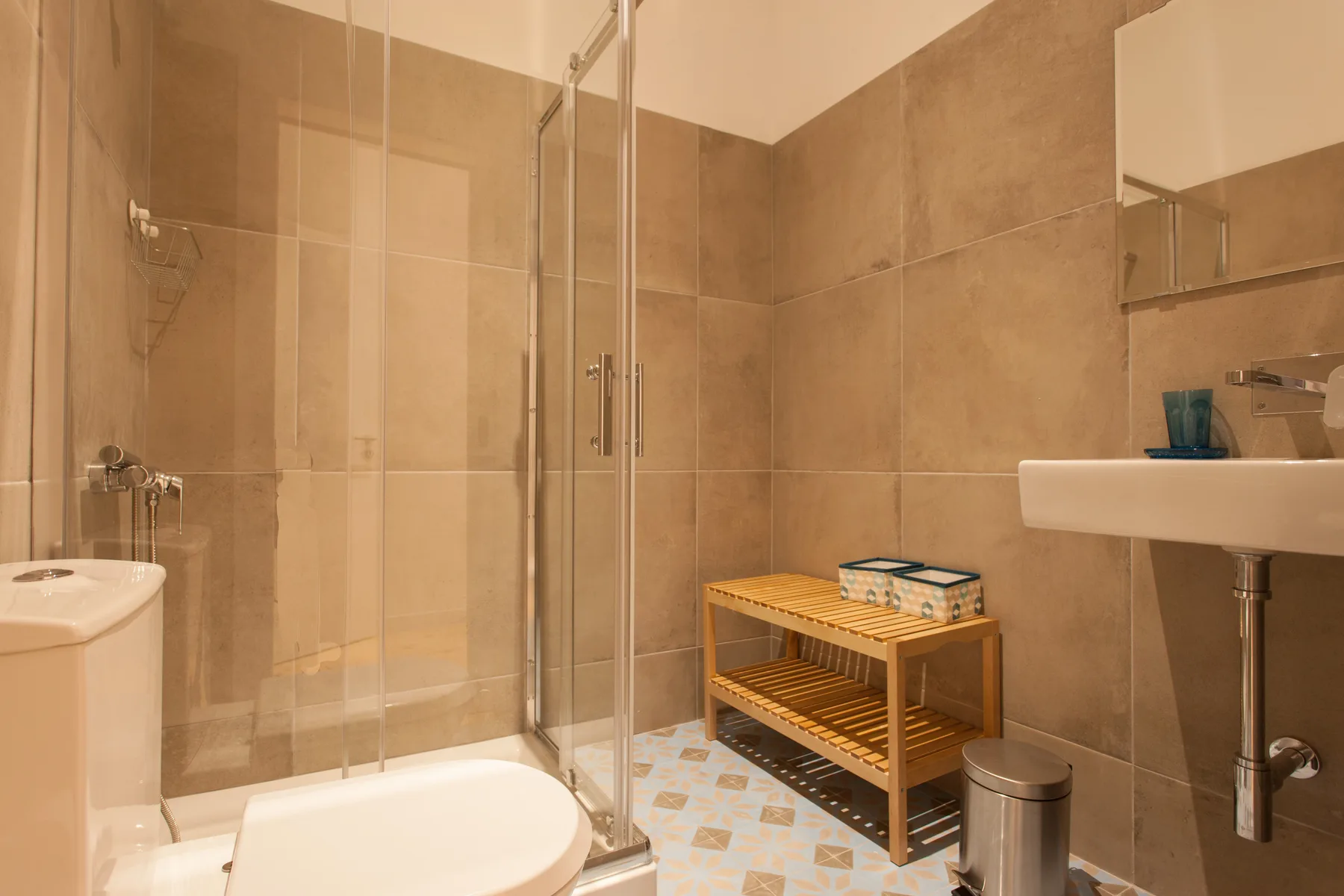 Un baño alicatado con ducha de cristal, lavabo y banco de almacenamiento de madera.
