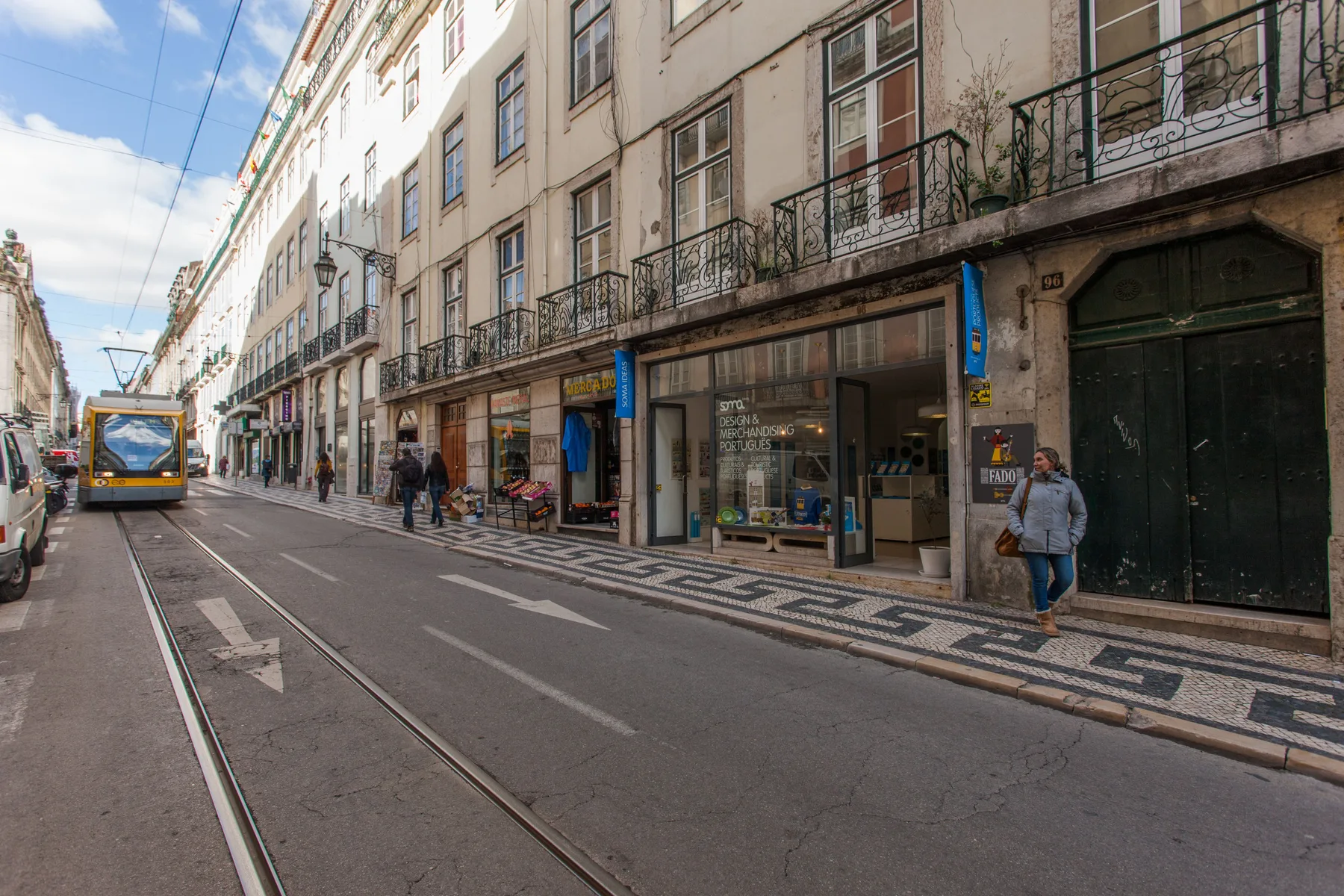 Una calle urbana con edificios de varias plantas, tiendas y un tranvía.