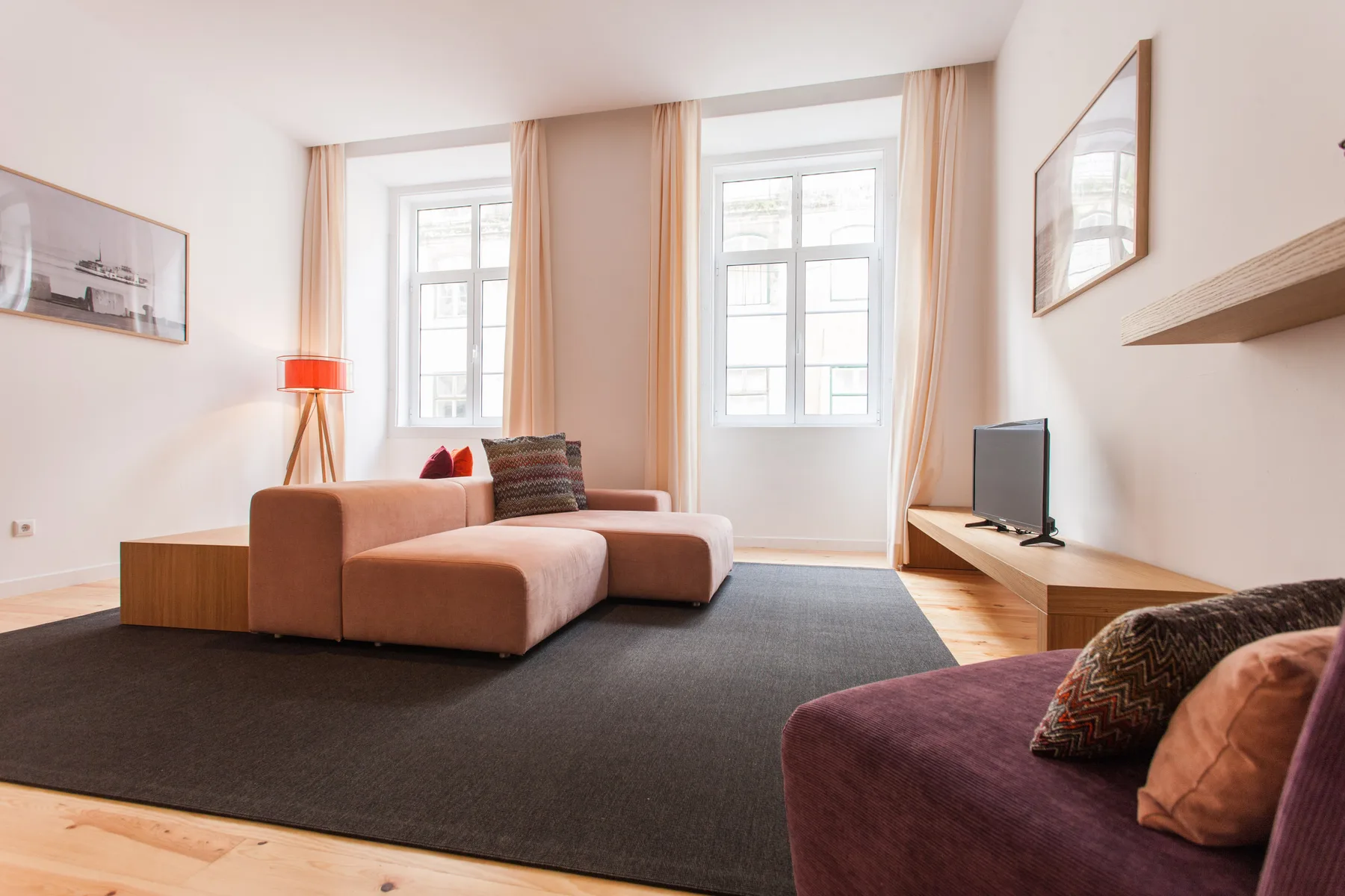Una sala luminosa con asientos, ventanas grandes y un televisor.