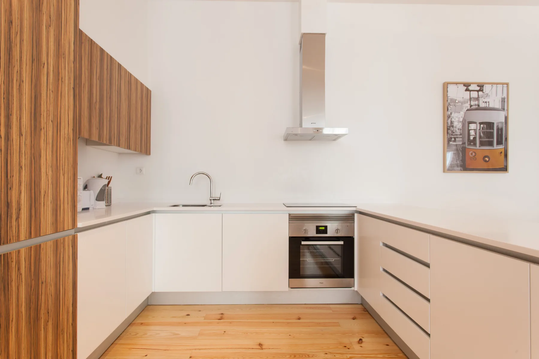 Una cocina luminosa con armarios blancos y suelo de madera.