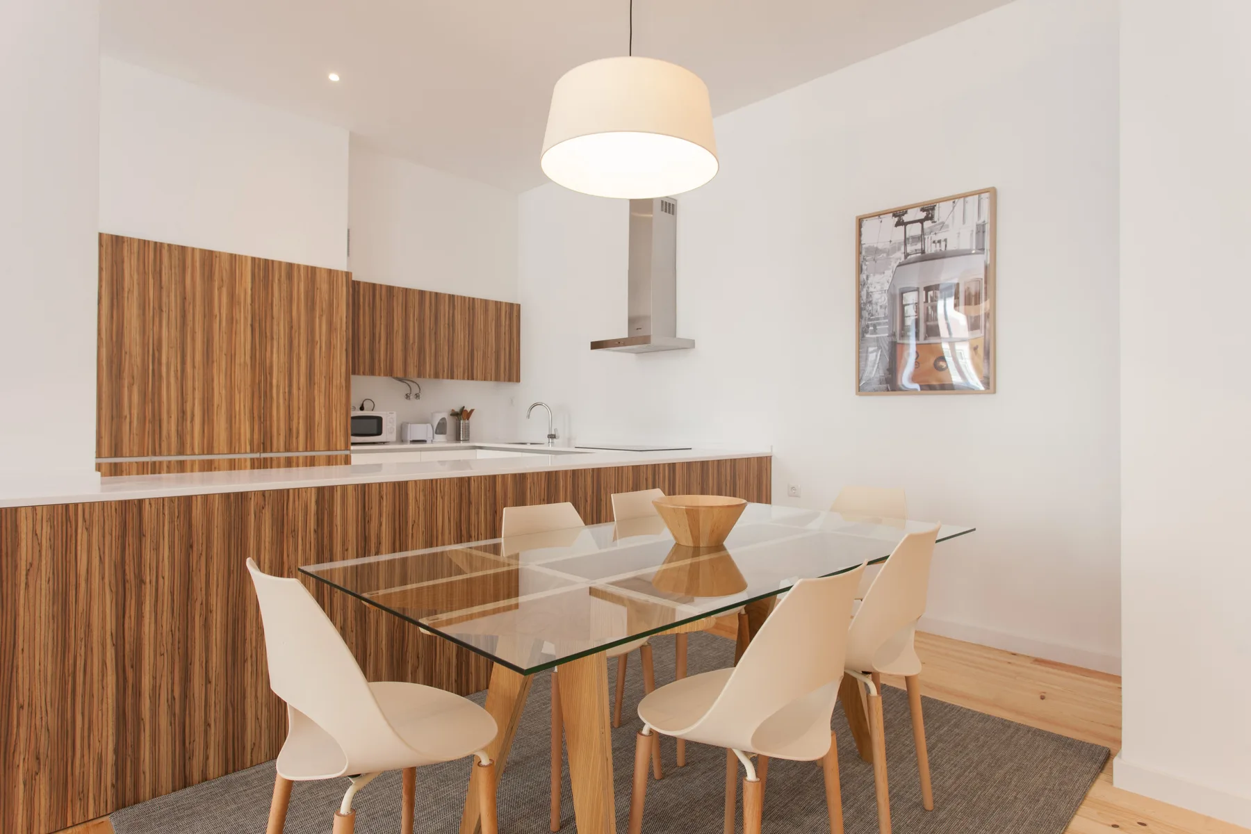 Comedor con una mesa de vidrio y una cocina con paneles de madera.